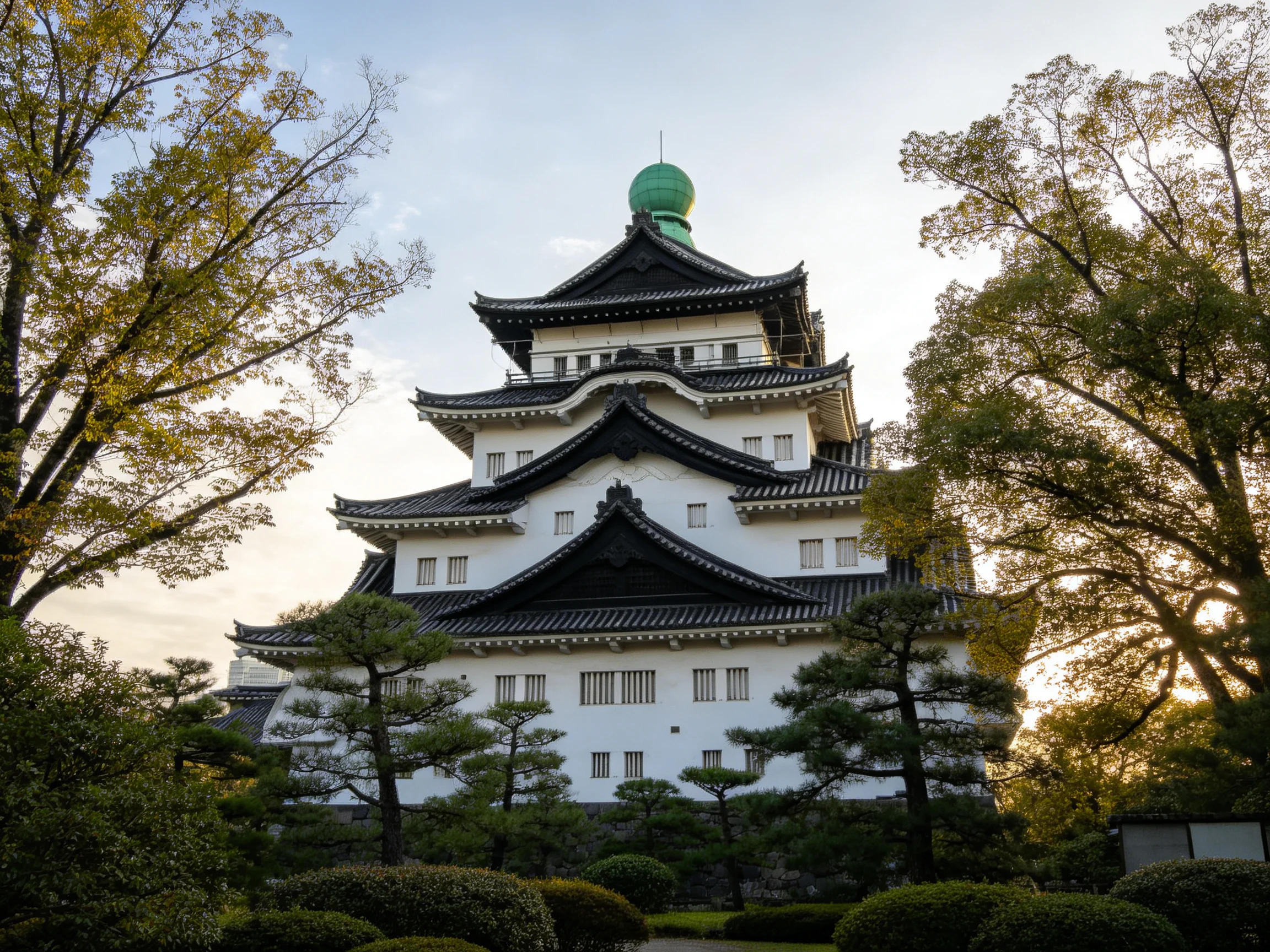 A traditional white castle tower with black roofs and a green dome surrounded by trees