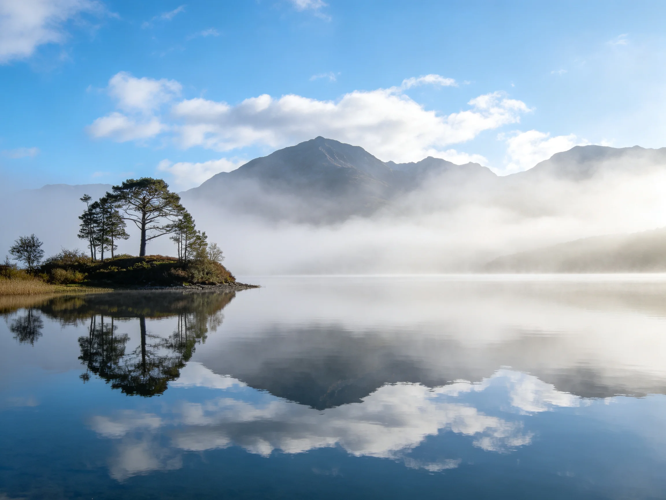 A tranquil lake reflects misty mountains and a tree - filled island