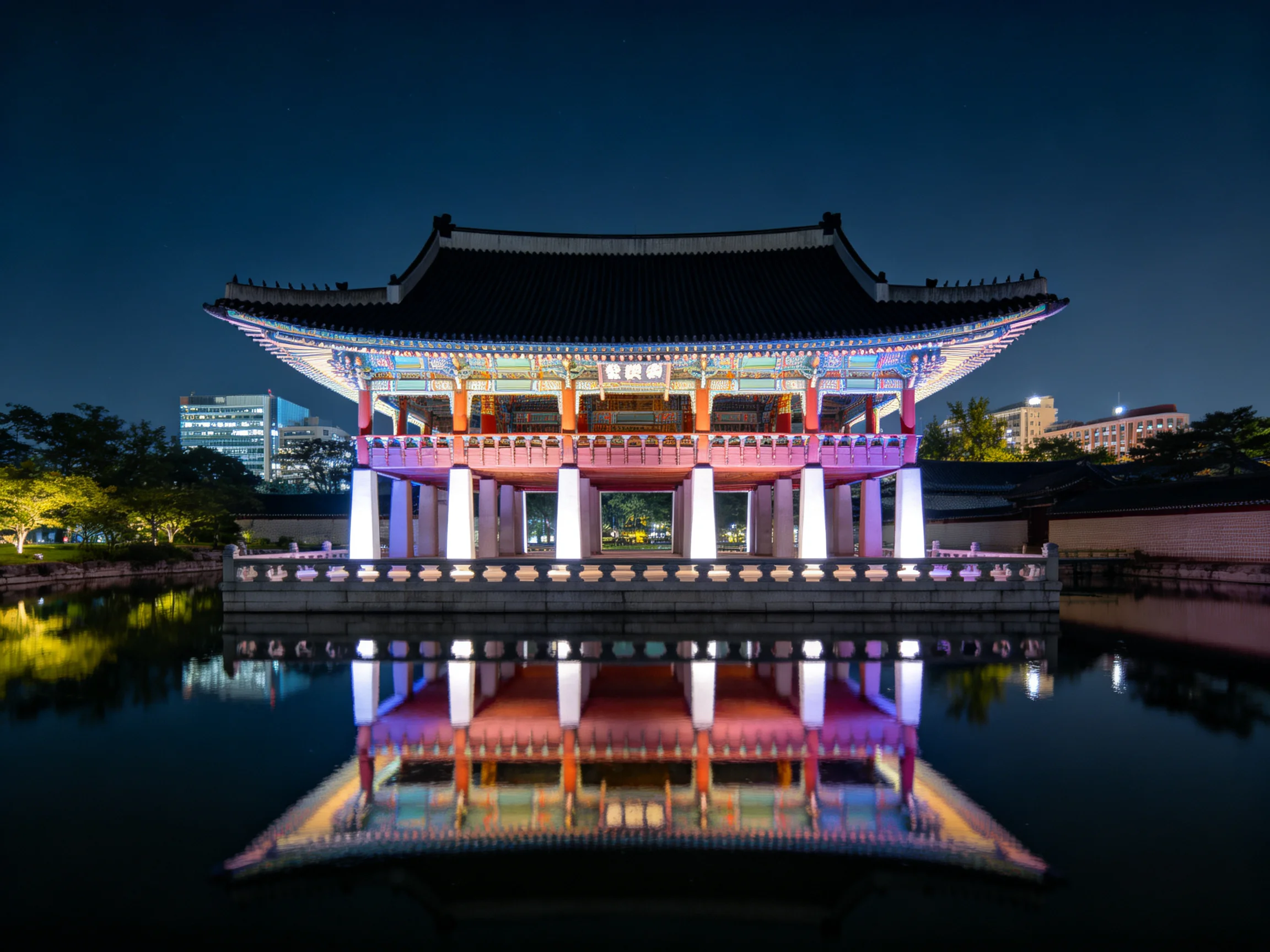A vibrantly lit traditional pavilion reflecting in calm water at night