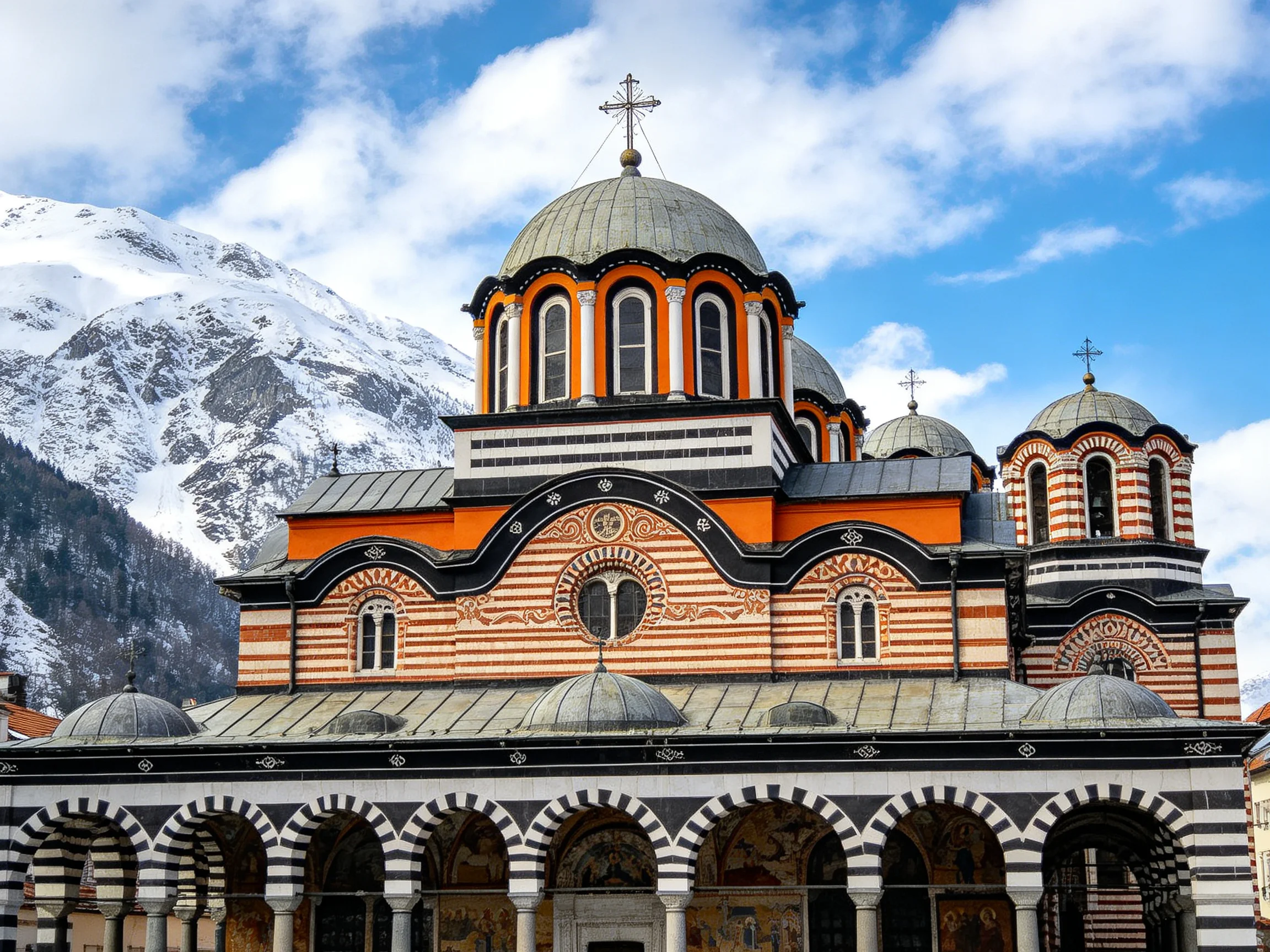 A vibrantly striped Orthodox church with domed towers near snow-capped mountains
