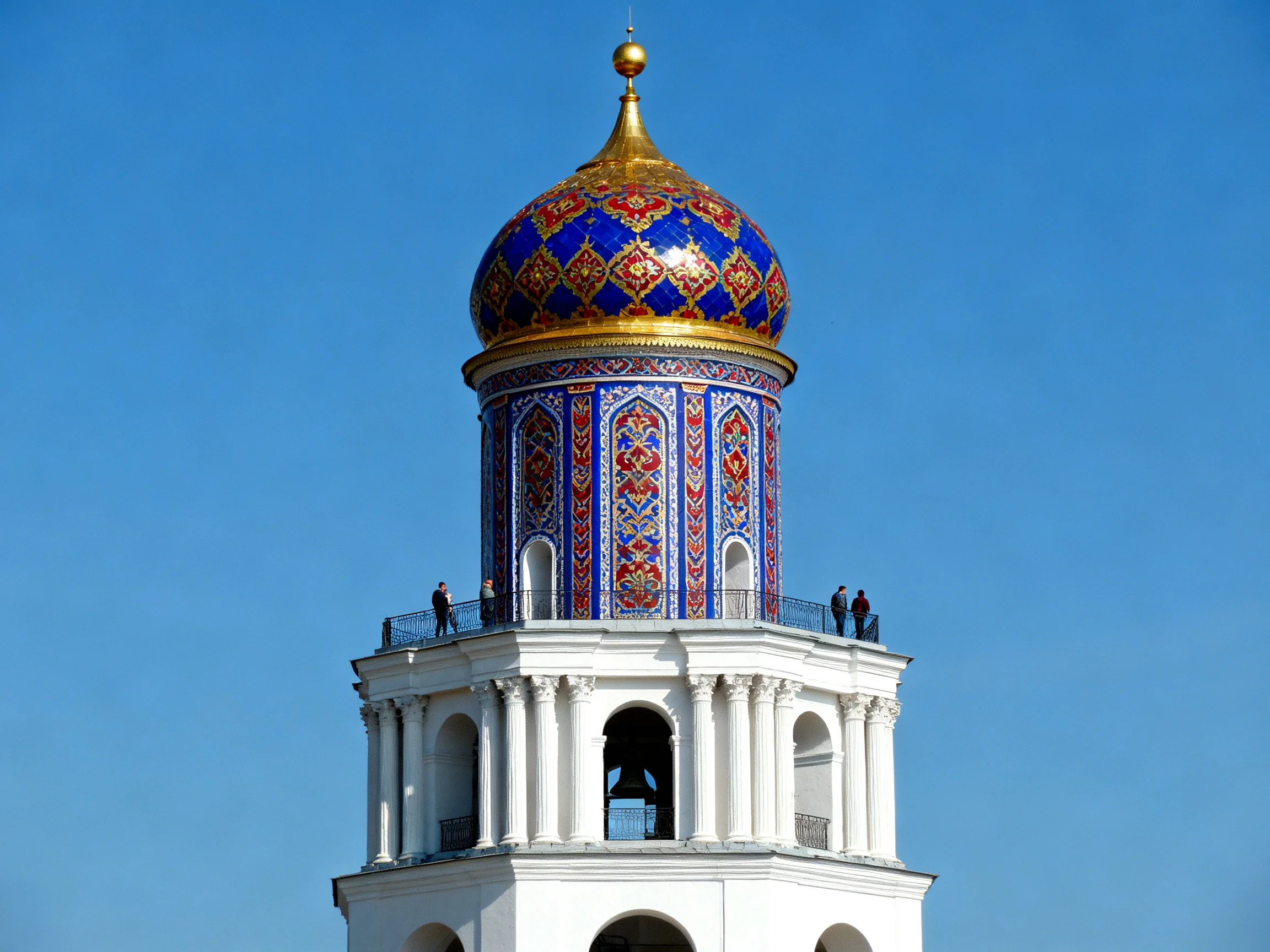 A vibrantly tiled tower with golden dome against clear blue sky