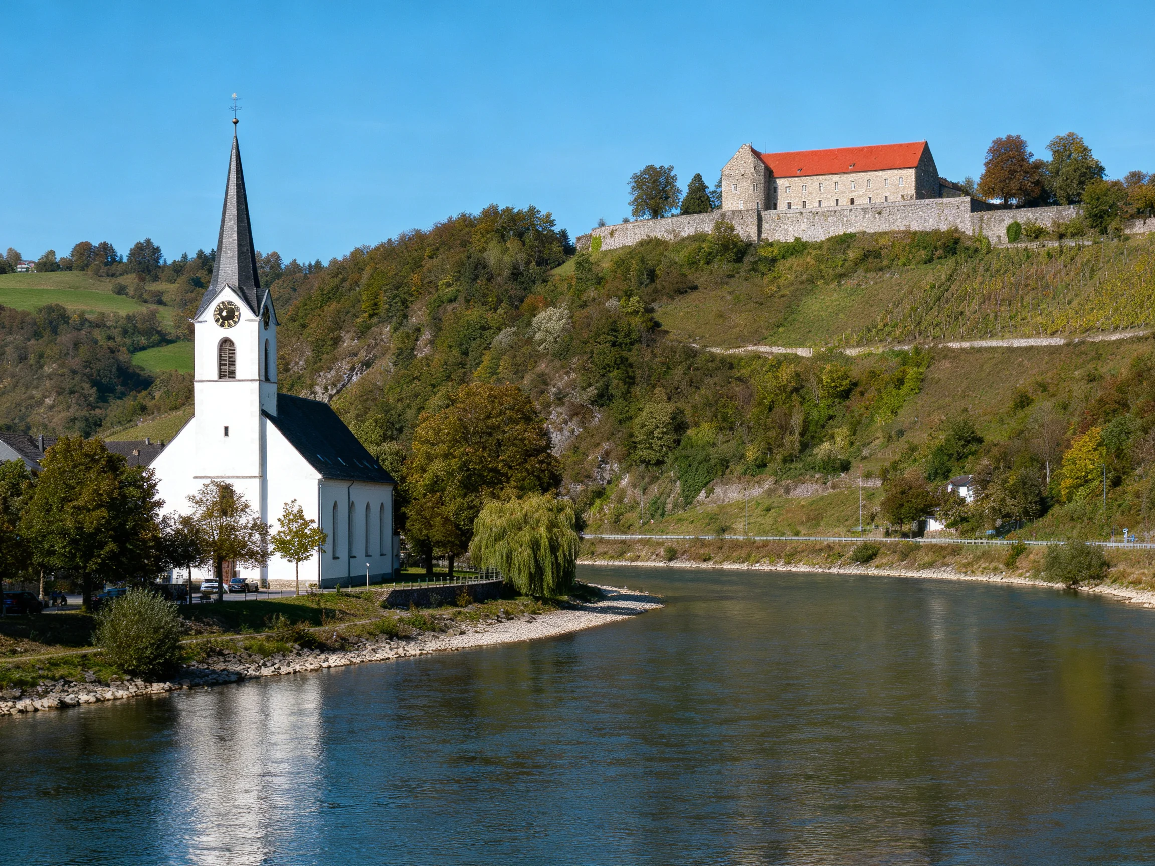 A white church beside a calm river near a red-roofed fortress