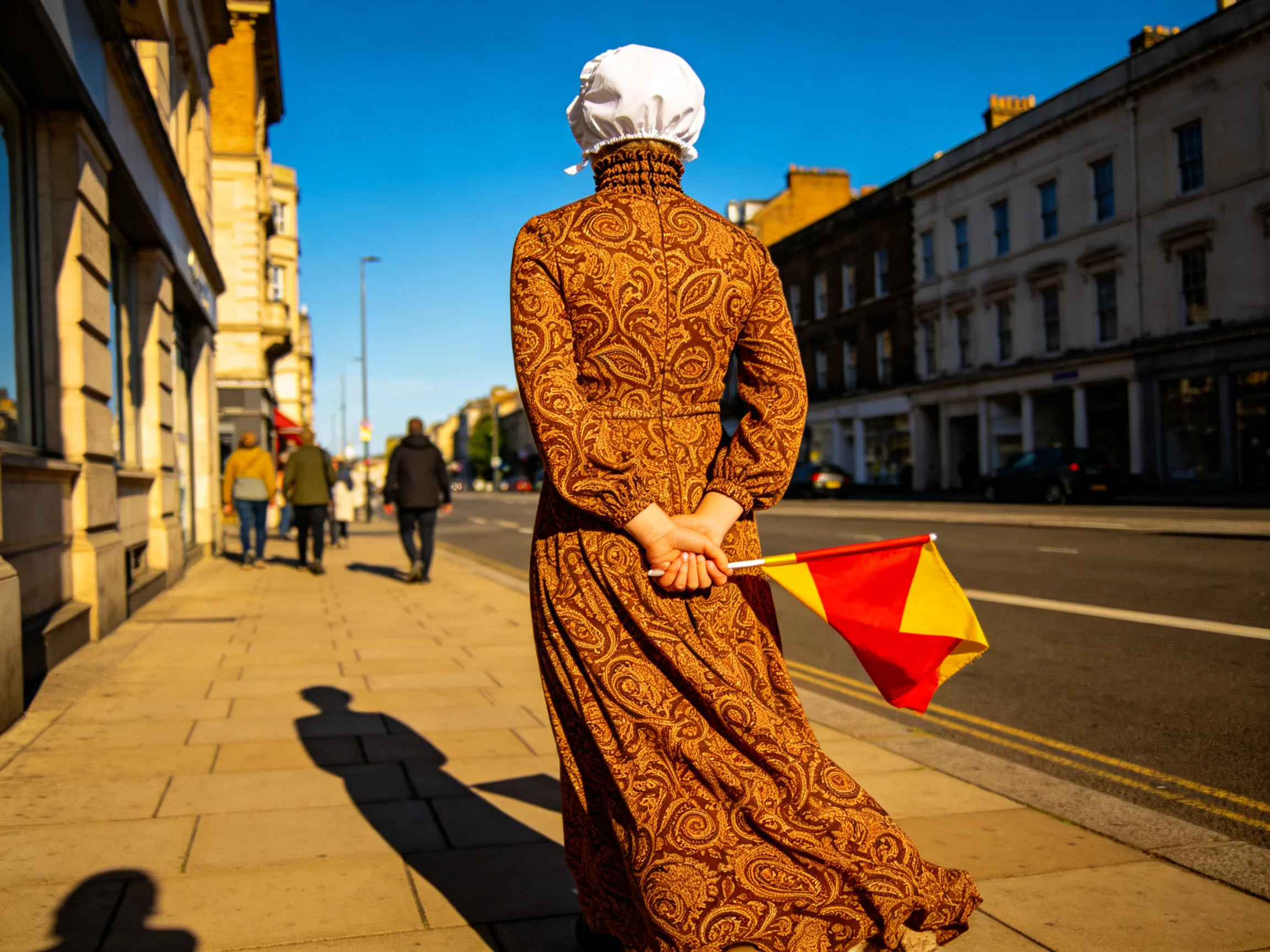 A woman in an ornate brown dress walks down a sunny city street