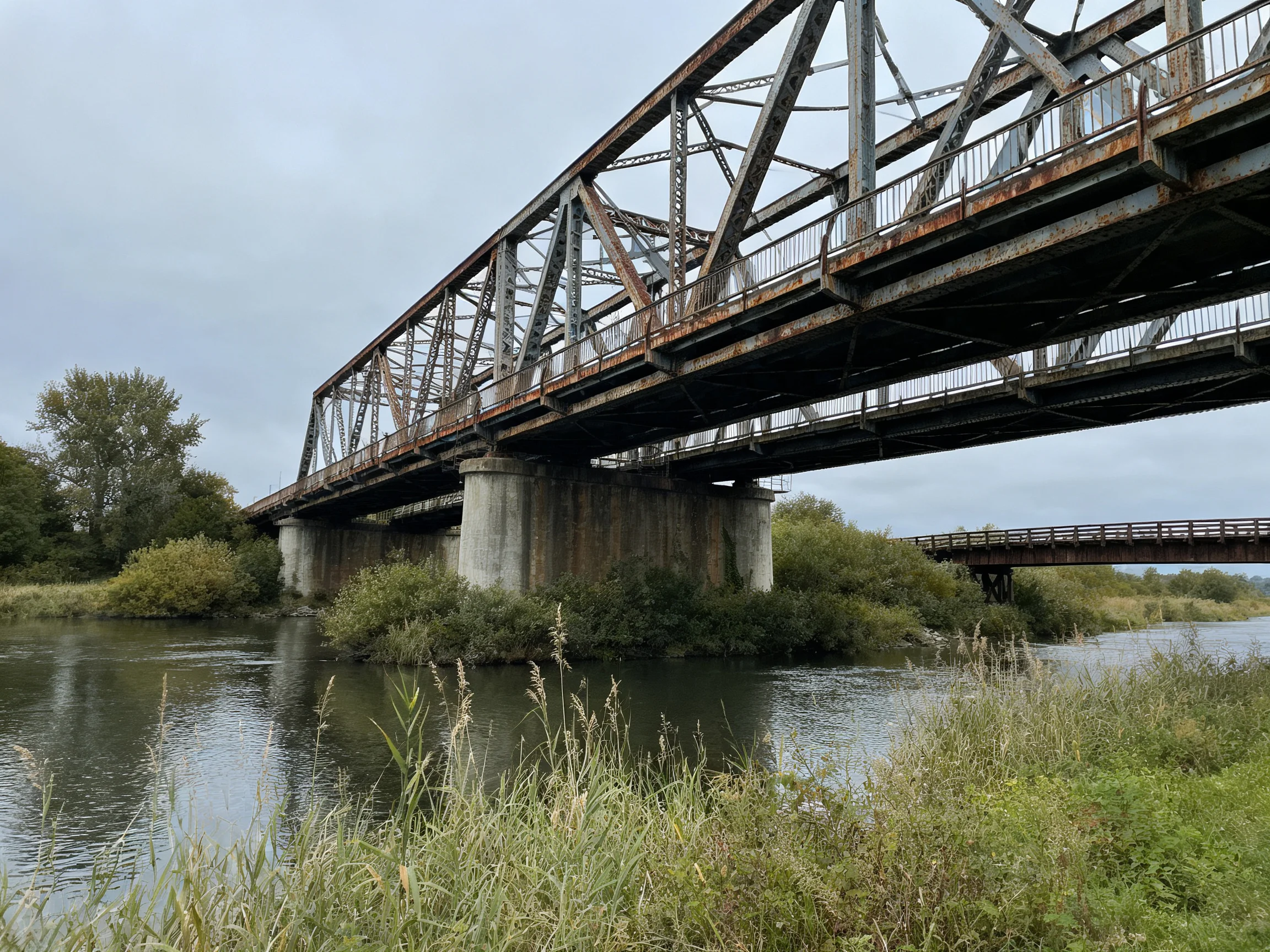 An aged steel truss bridge spans a calm river with lush vegetation