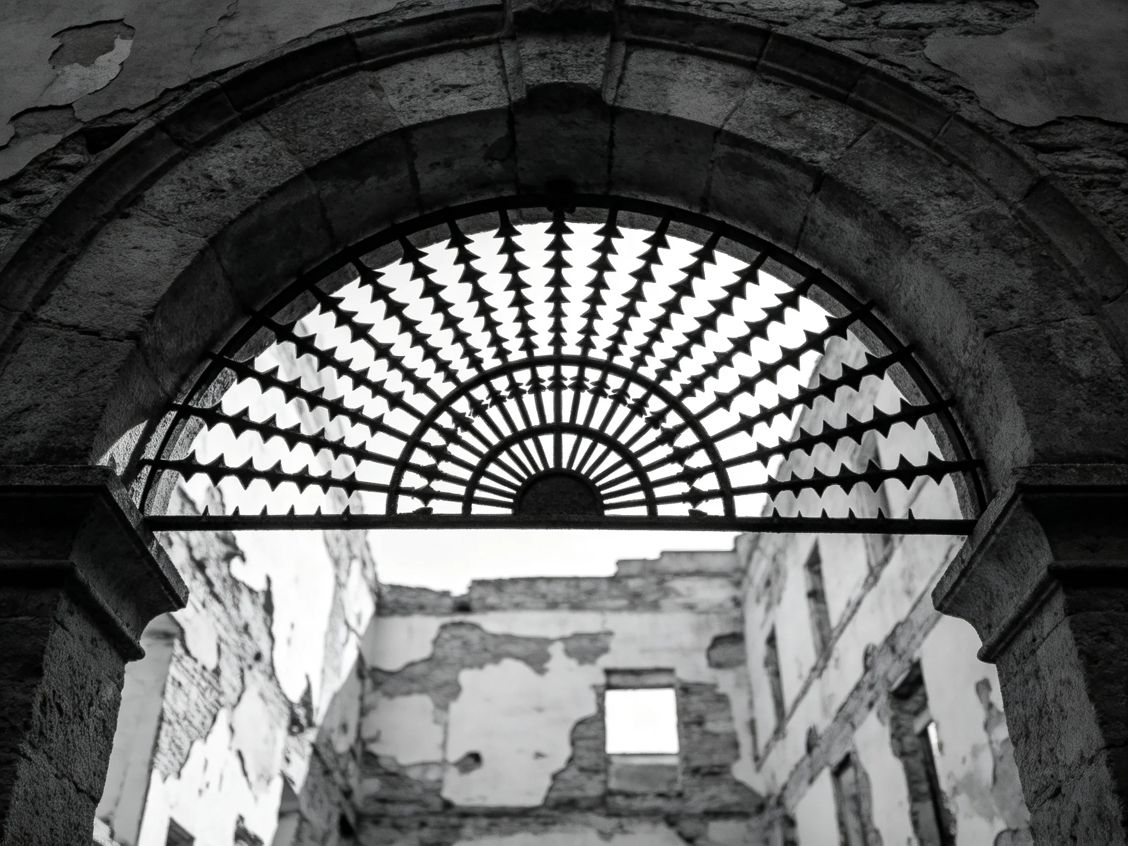 An aged stone arch frames a weathered iron grille over crumbling ruins