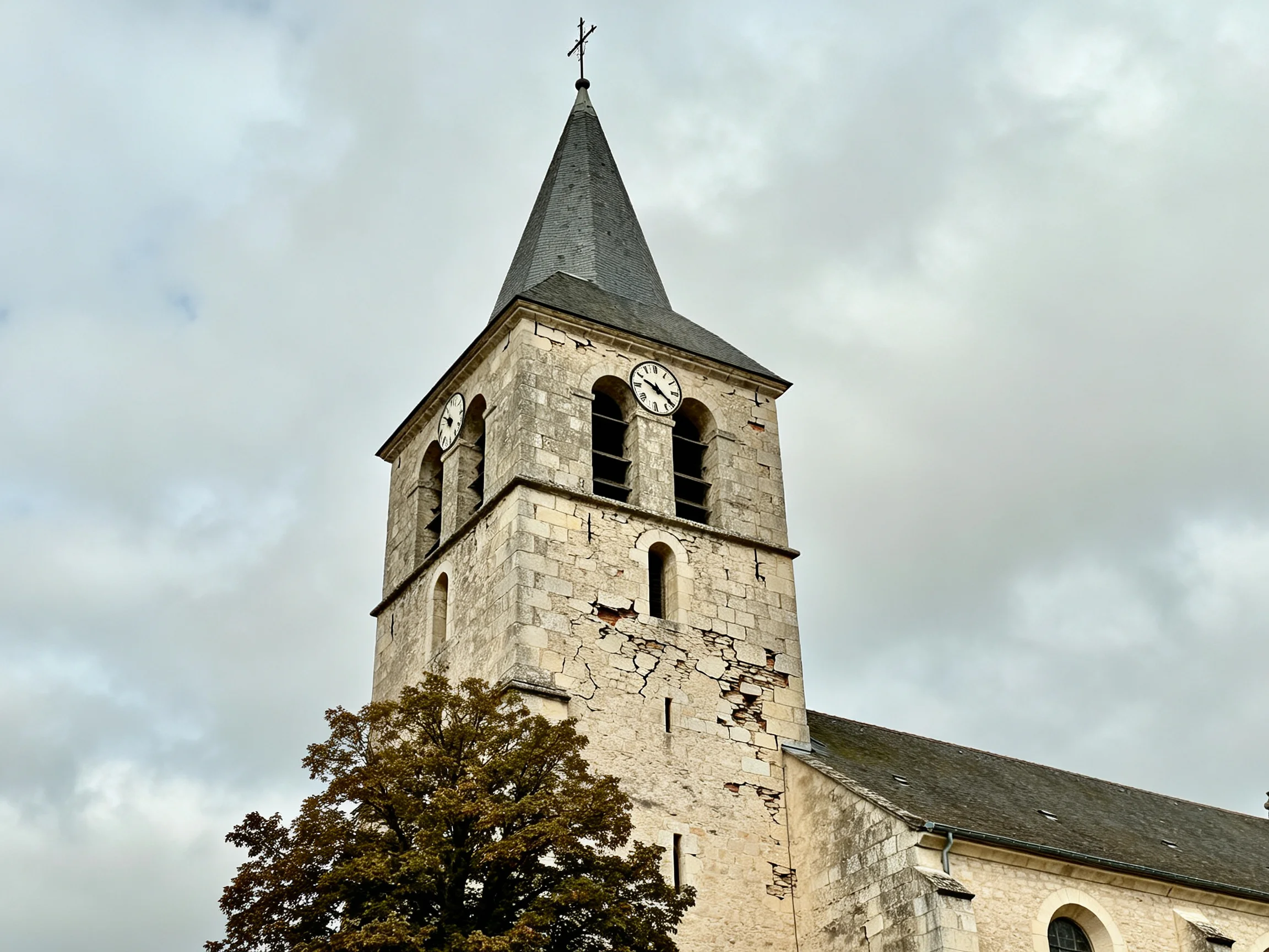 An aged stone church tower with clocks, cross