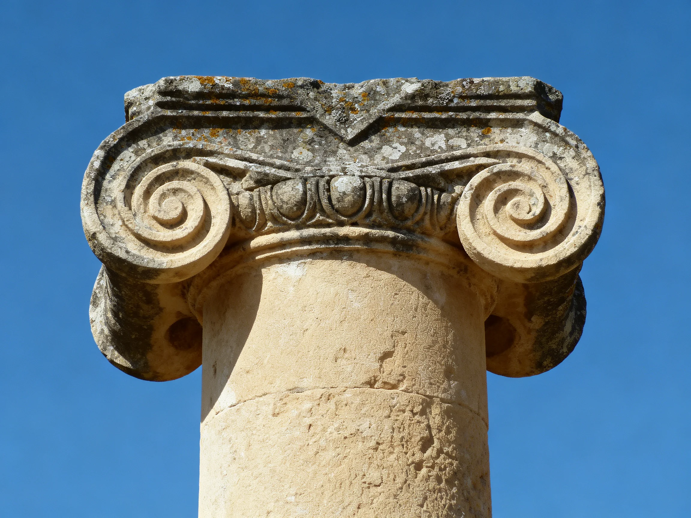 An aged stone column capital with ornate scroll designs