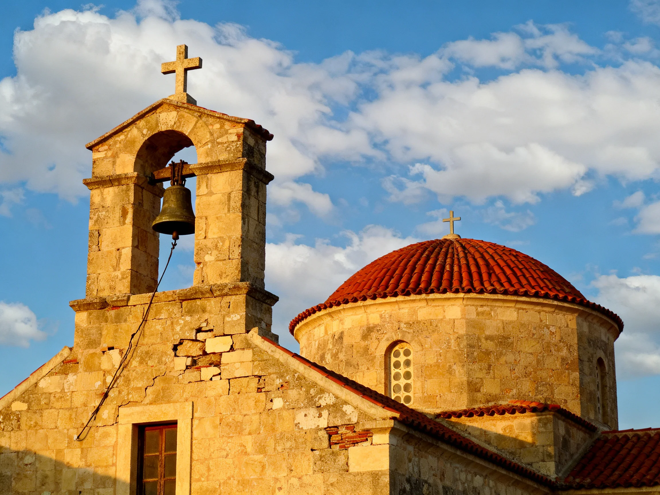 An ancient stone church with bell tower and red-tiled dome