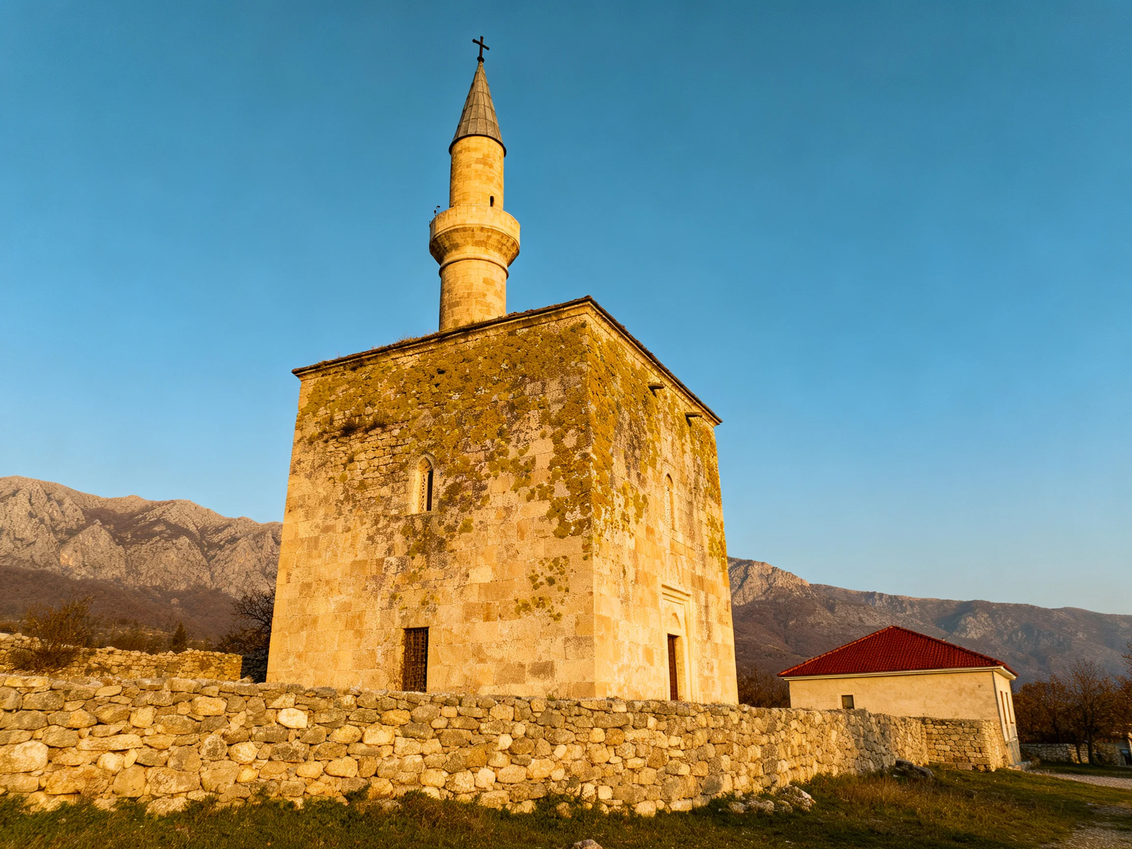 An ancient stone mosque with a tall minaret near mountainous terrain