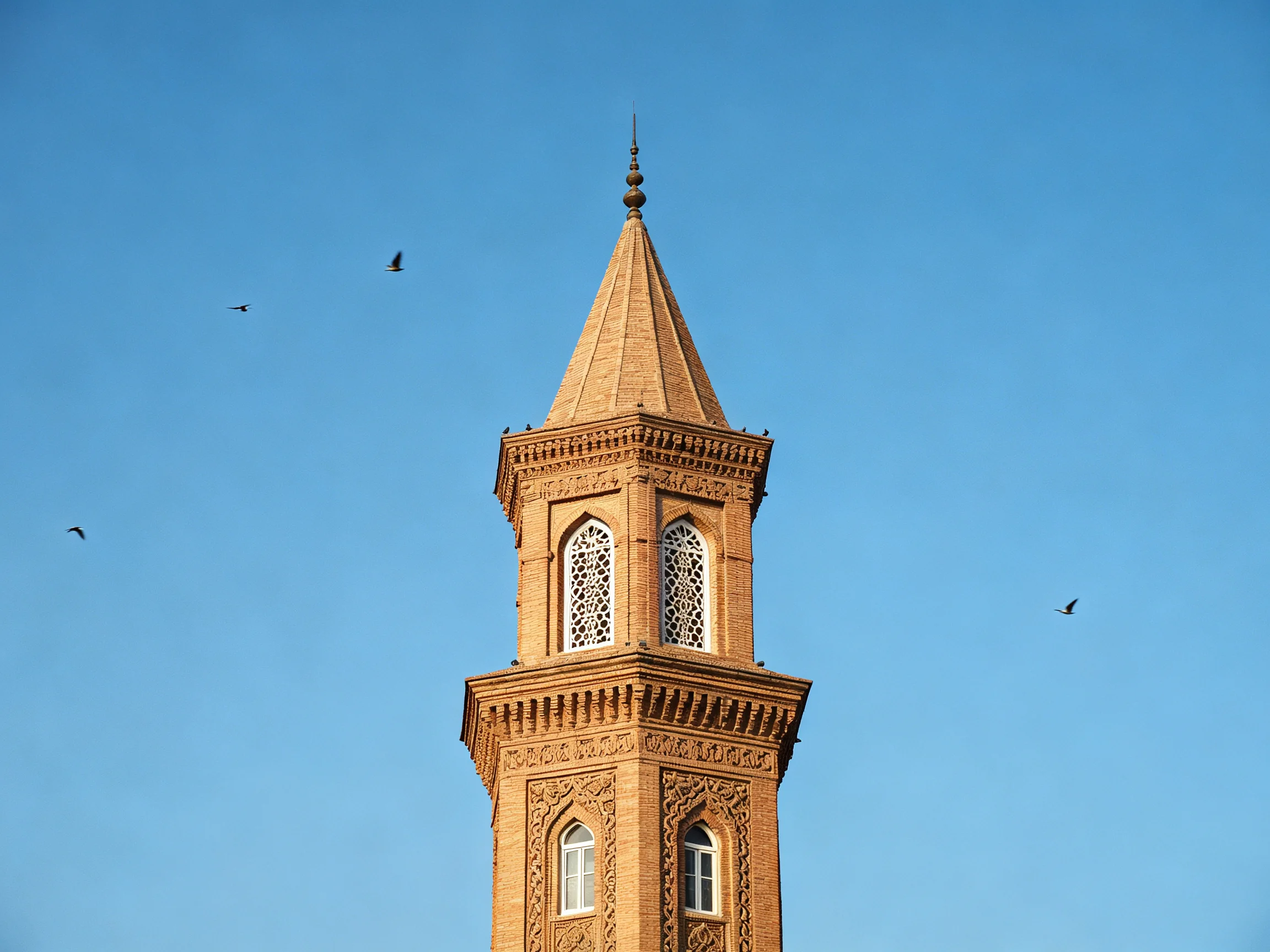 An ornate brick minaret with decorative patterns stands against a clear blue sky