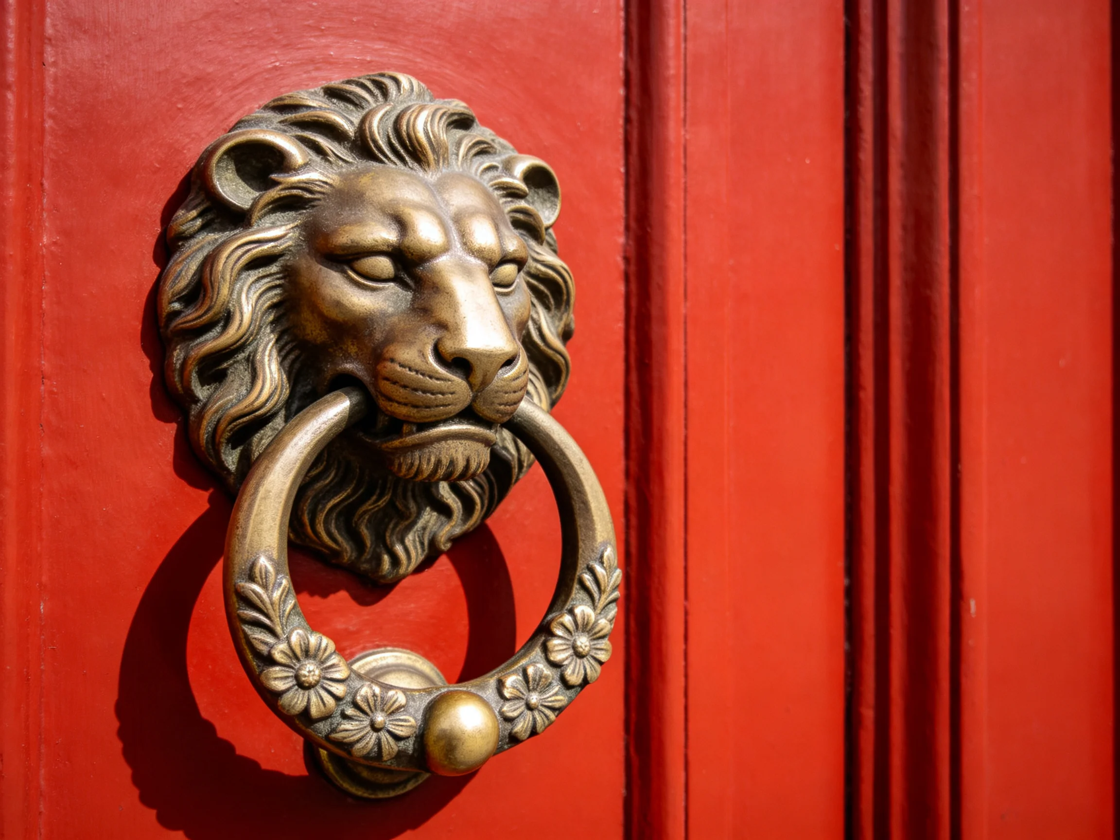 An ornate bronze lion door knocker on a vivid red wooden door