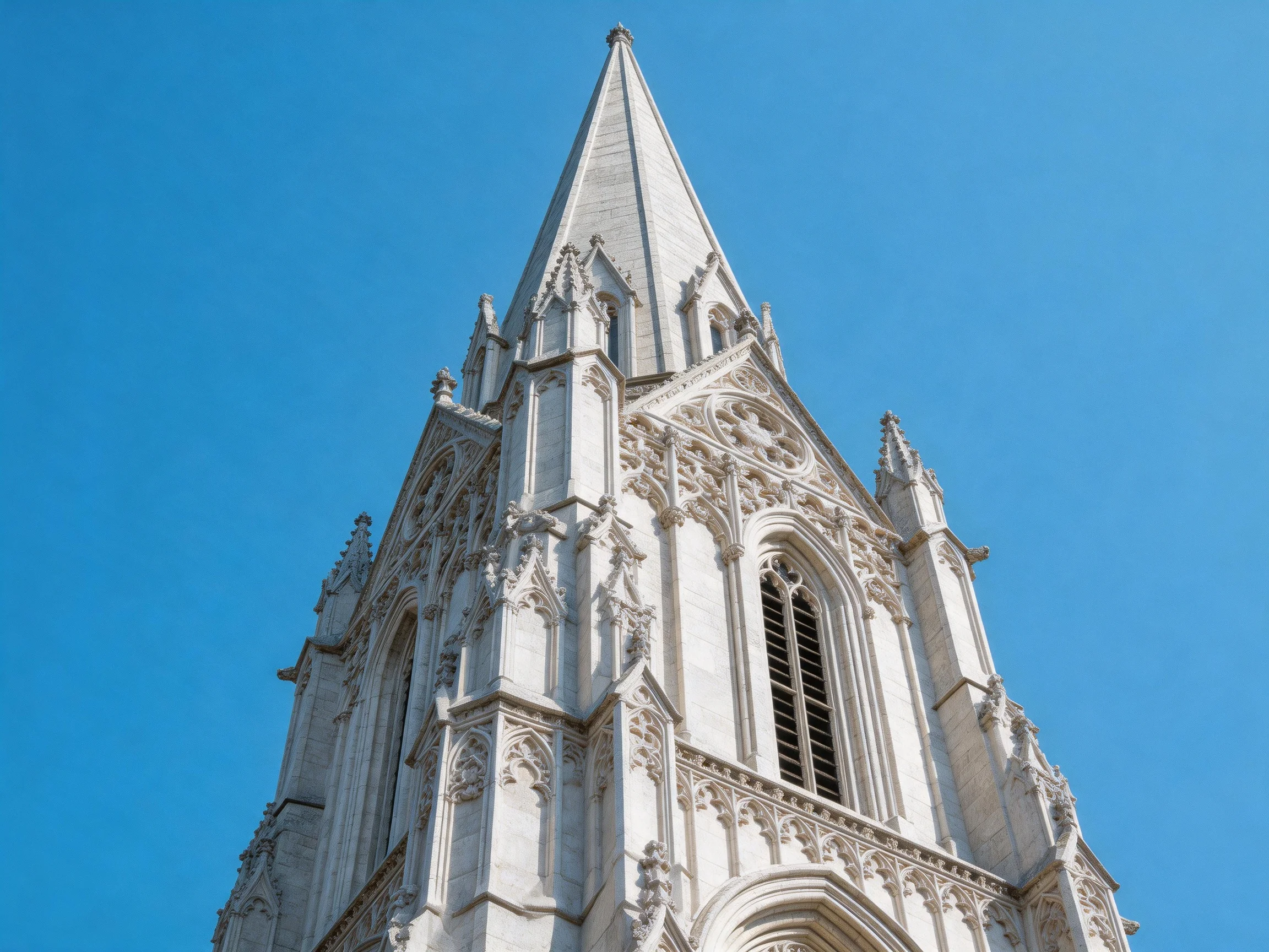 An ornate white stone church tower with pointed spire under clear blue sky
