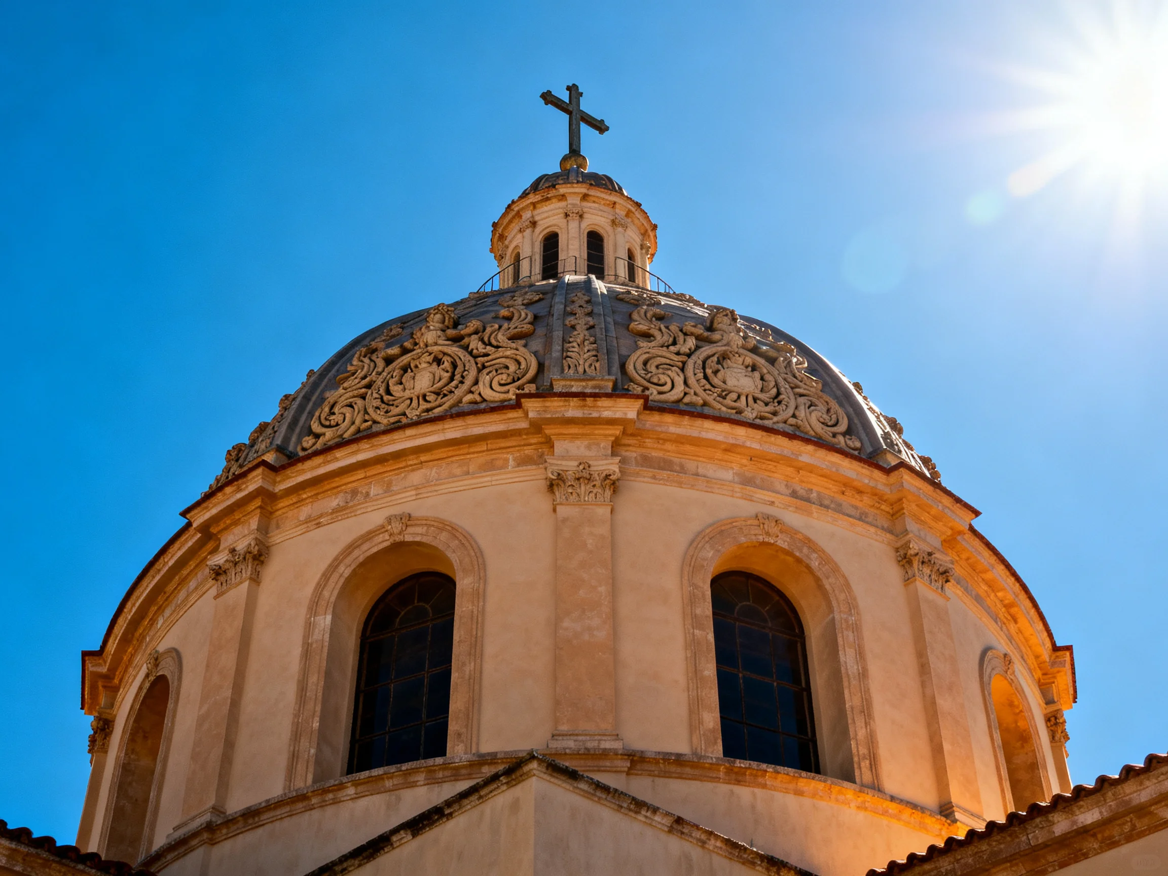 An ornately decorated church dome topped with a cross under a clear blue sky