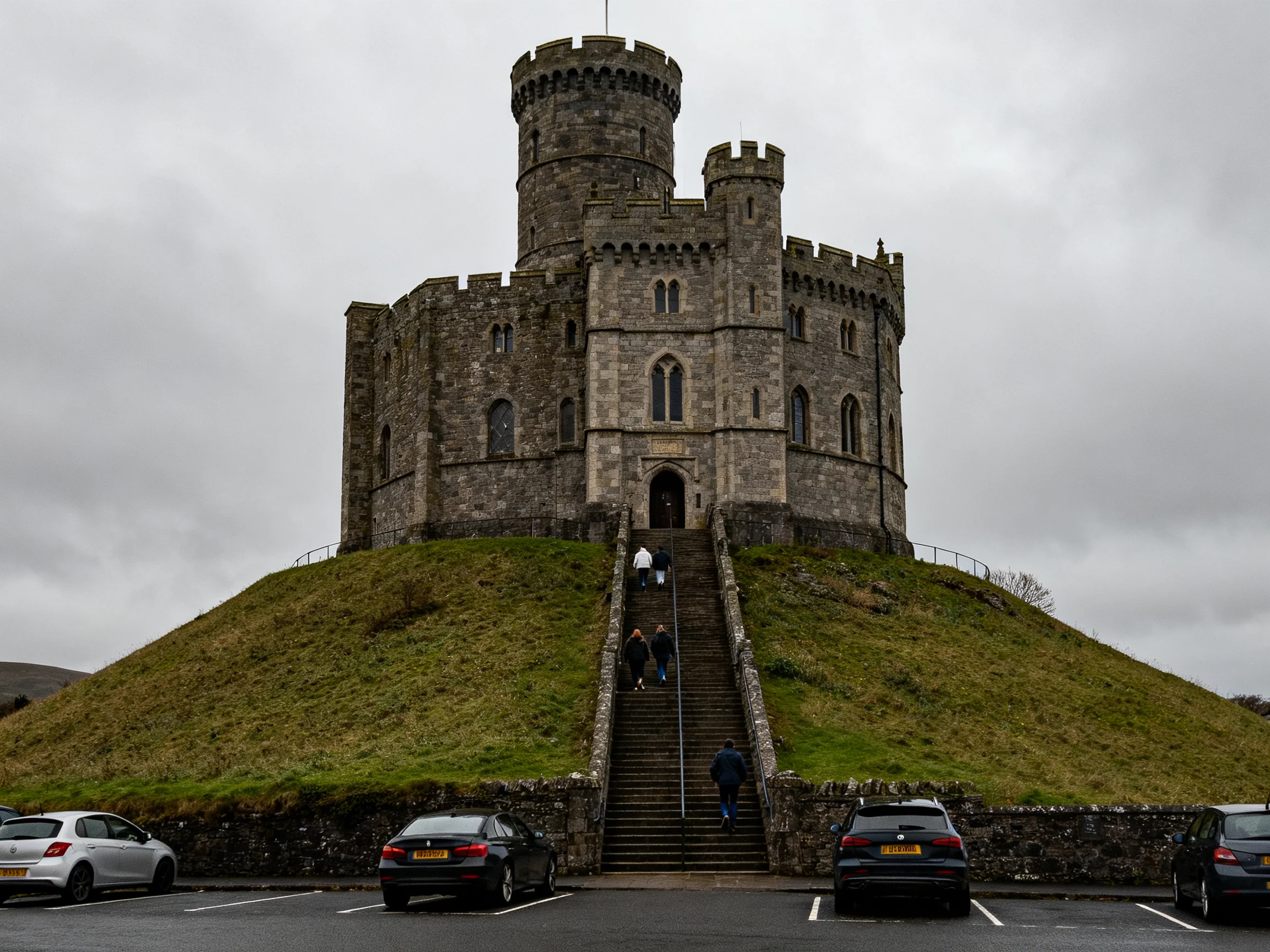 Ancient stone castle atop a grassy mound with parked cars