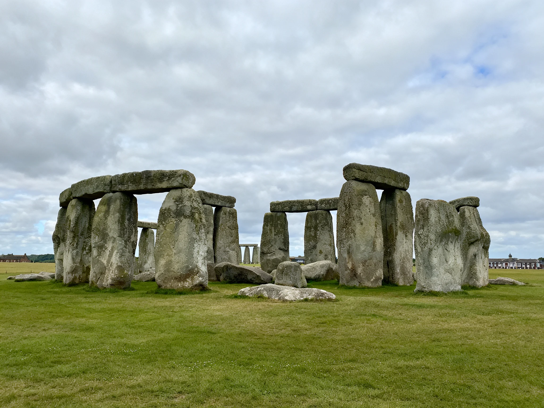 Ancient stone monument with massive grey stones on lush green grass under cloudy sky