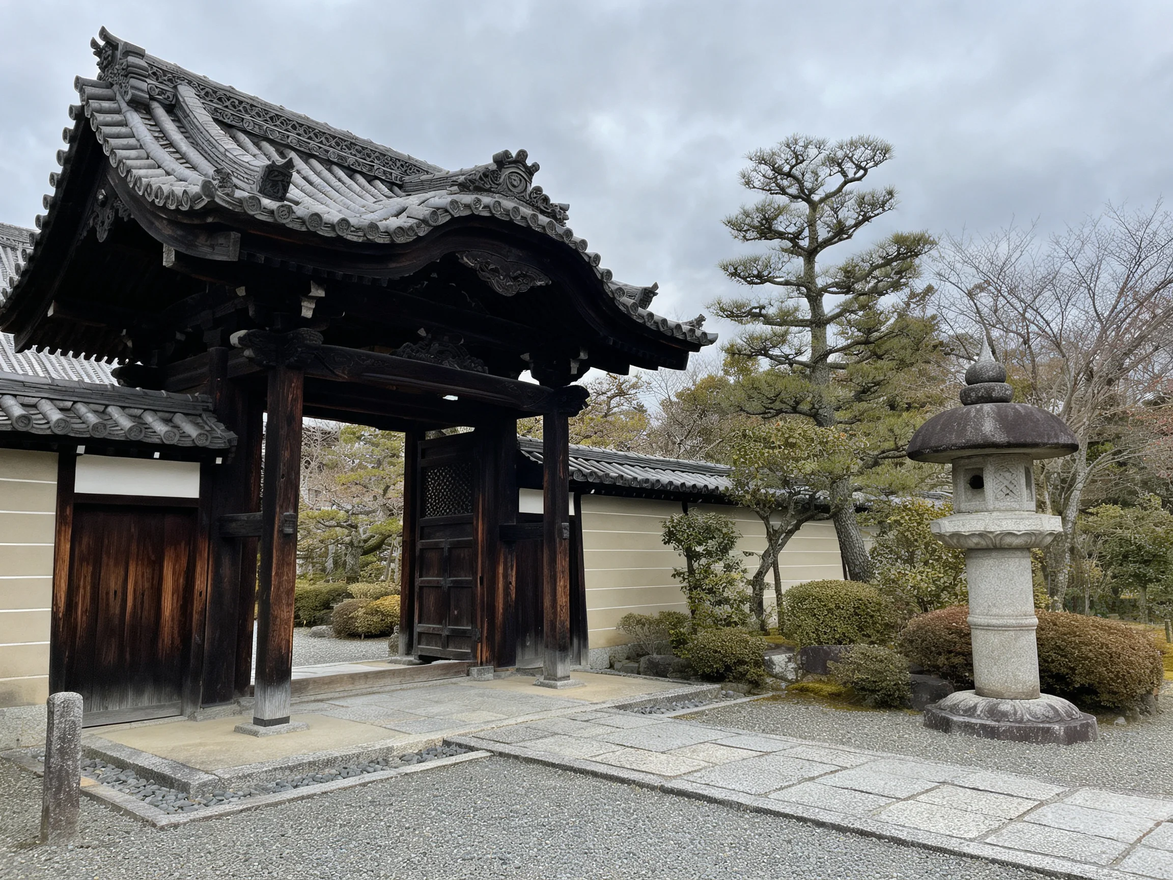 Ancient wooden gateway with ornate tiled roof near stone lantern