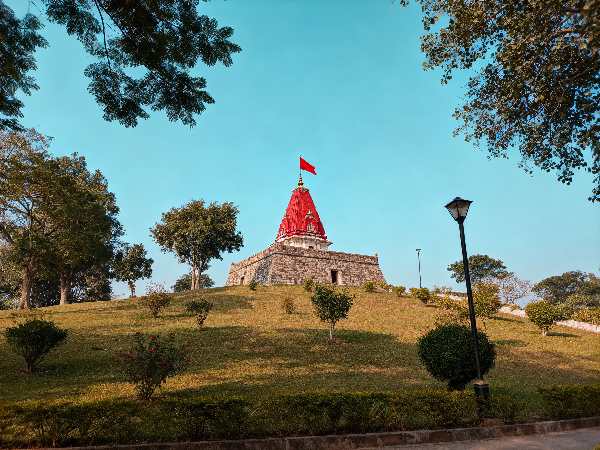 Astone temple with a bright red dome atop a grassy hill