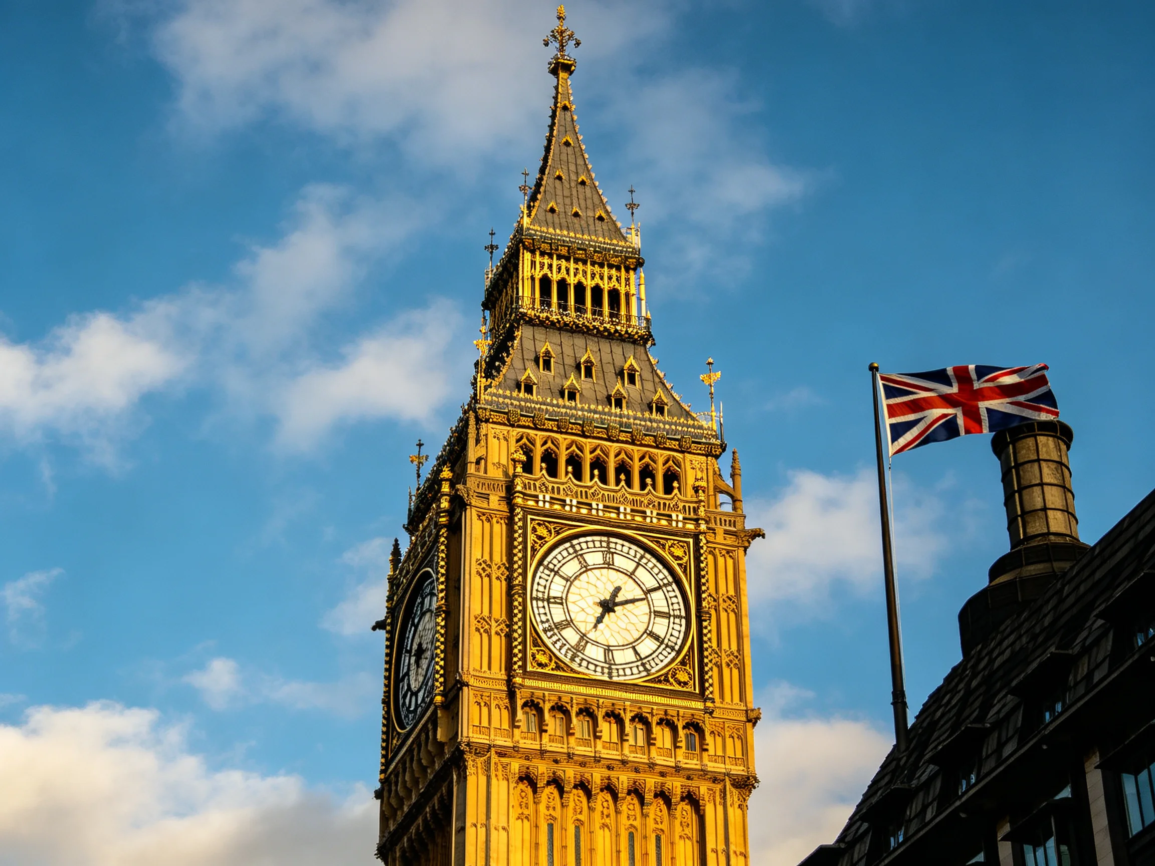 Big Ben clock tower with golden facade, Union Jack flag, and blue sky