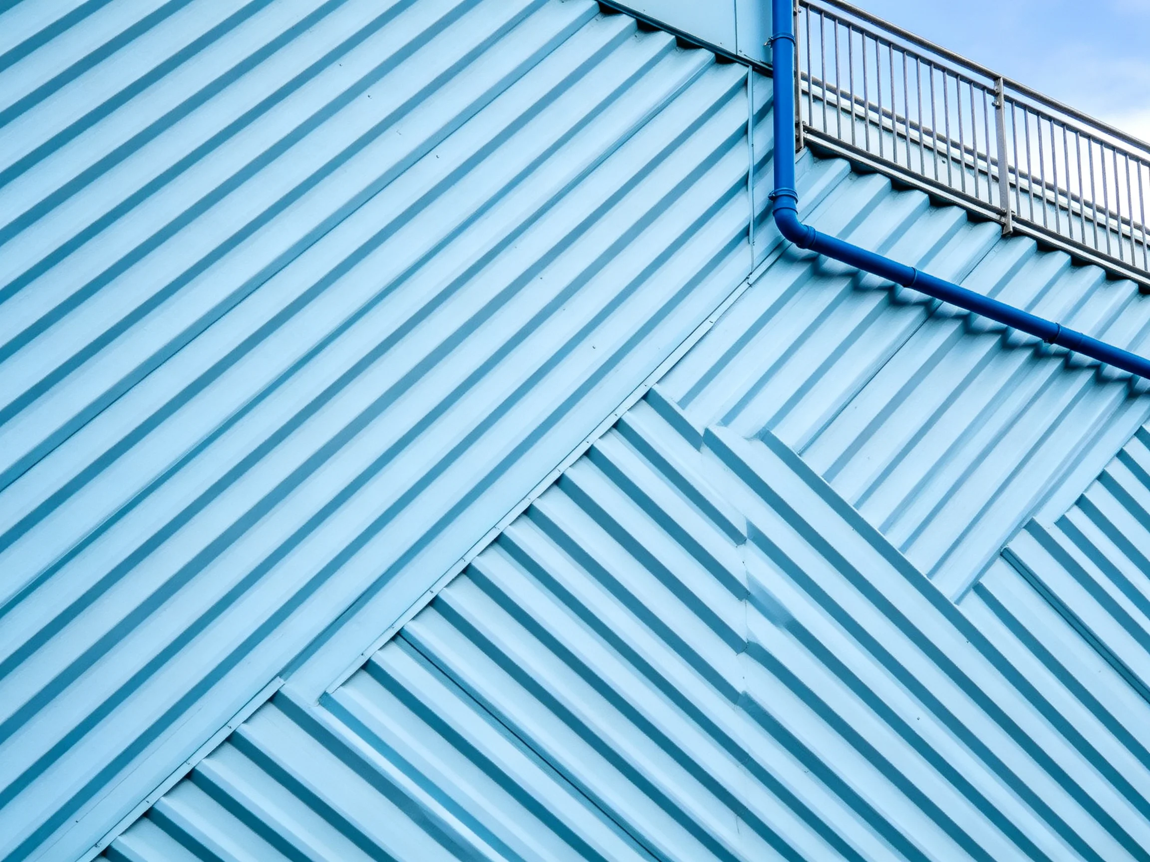 Blue corrugated wall with blue pipe and metal railing
