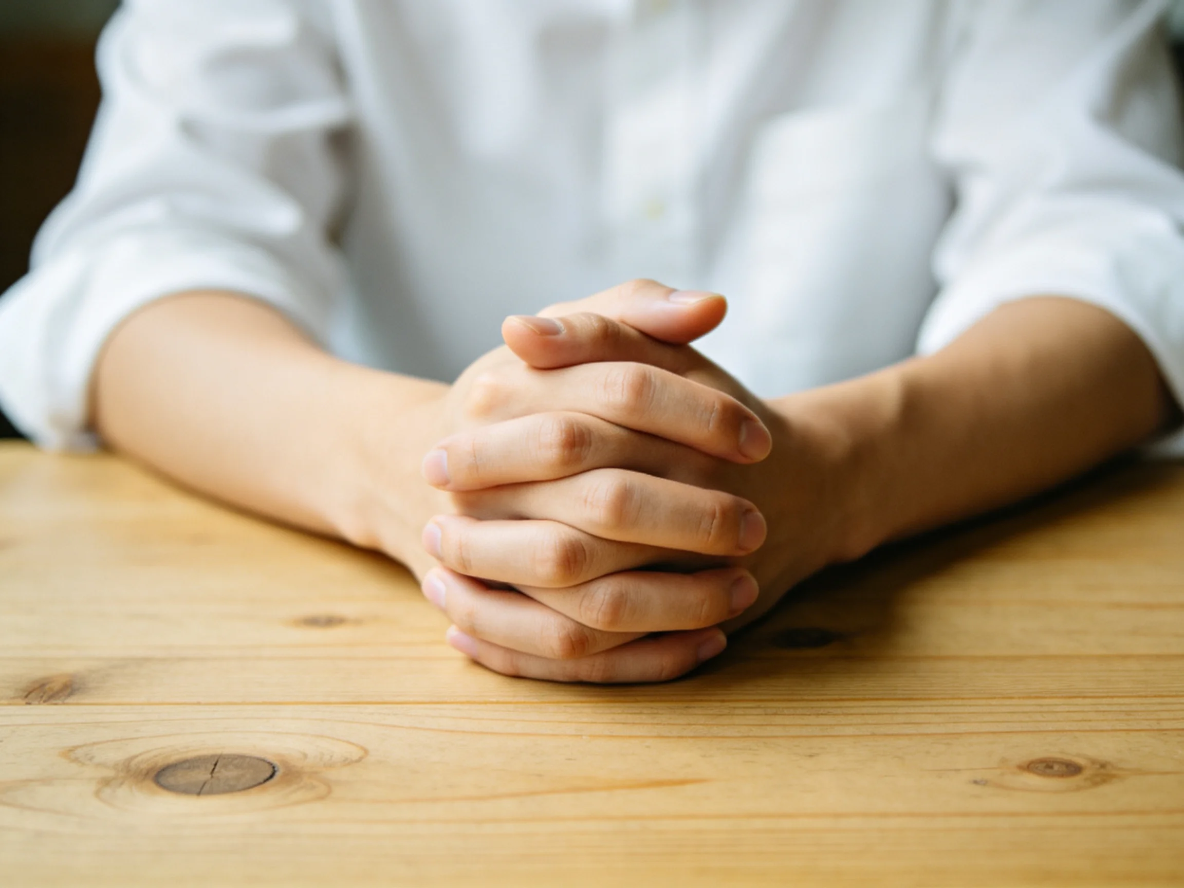 Clasped Hands on a Light Wood Table with White Clothing