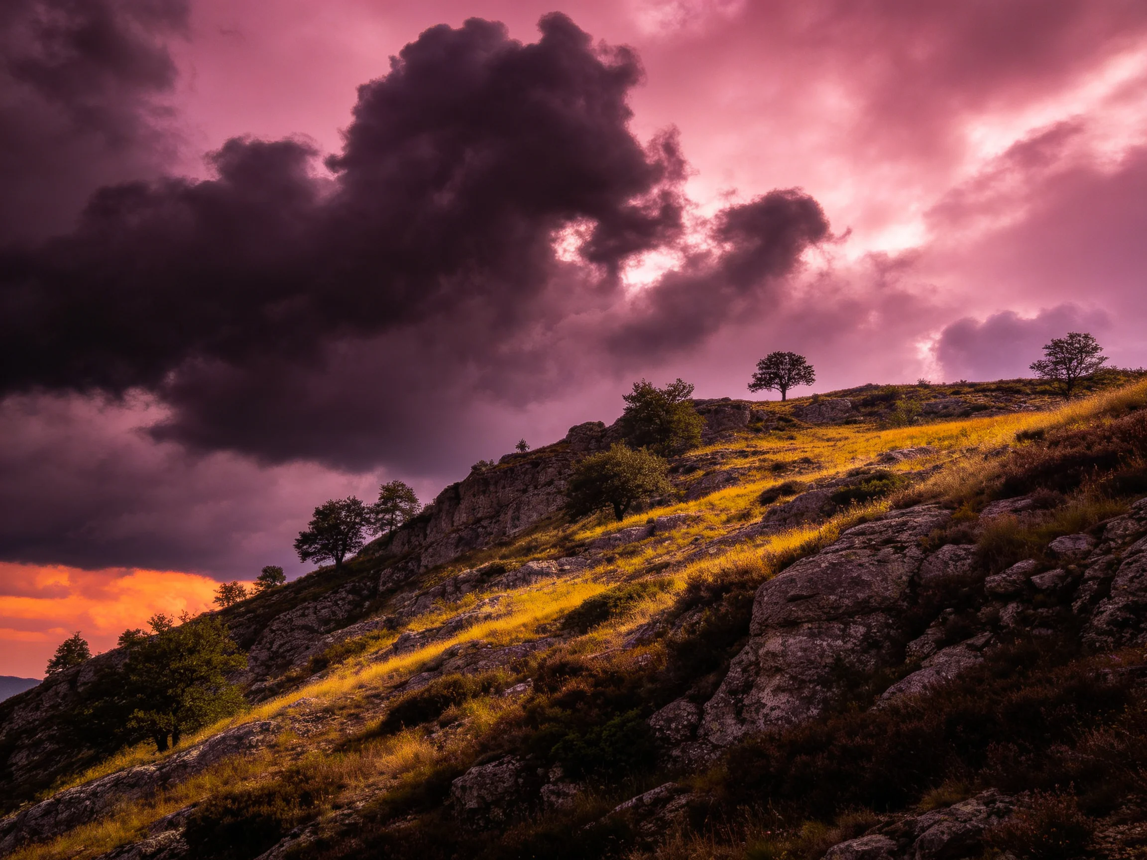 Dramatic sunset over rocky hillside with scattered trees