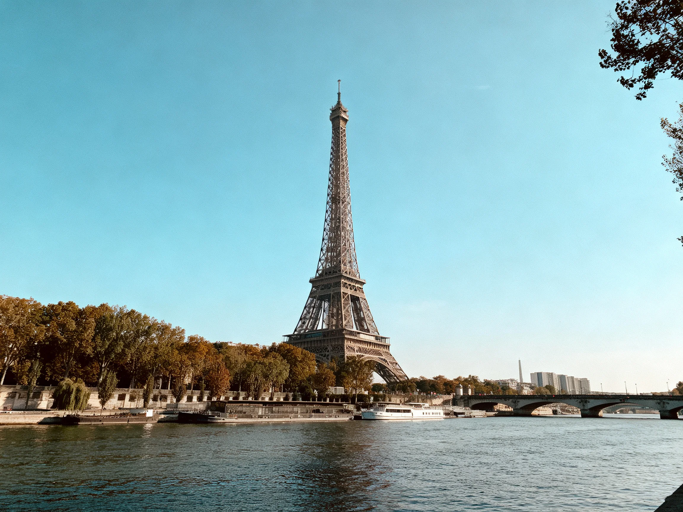 Eiffel Tower stands tall by a calm river with autumn trees
