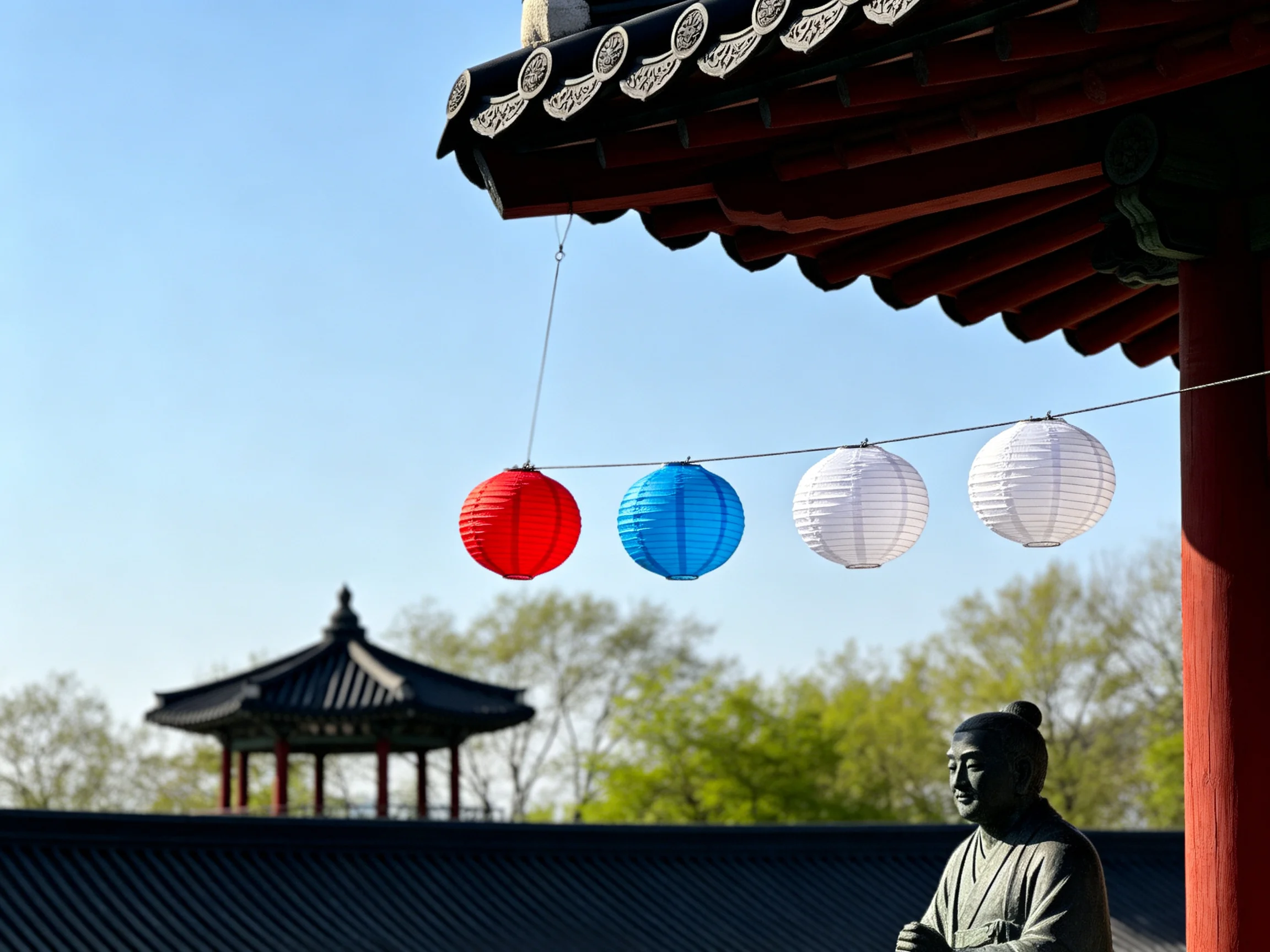 Four colorful paper lanterns near traditional East Asian architecture with a statue