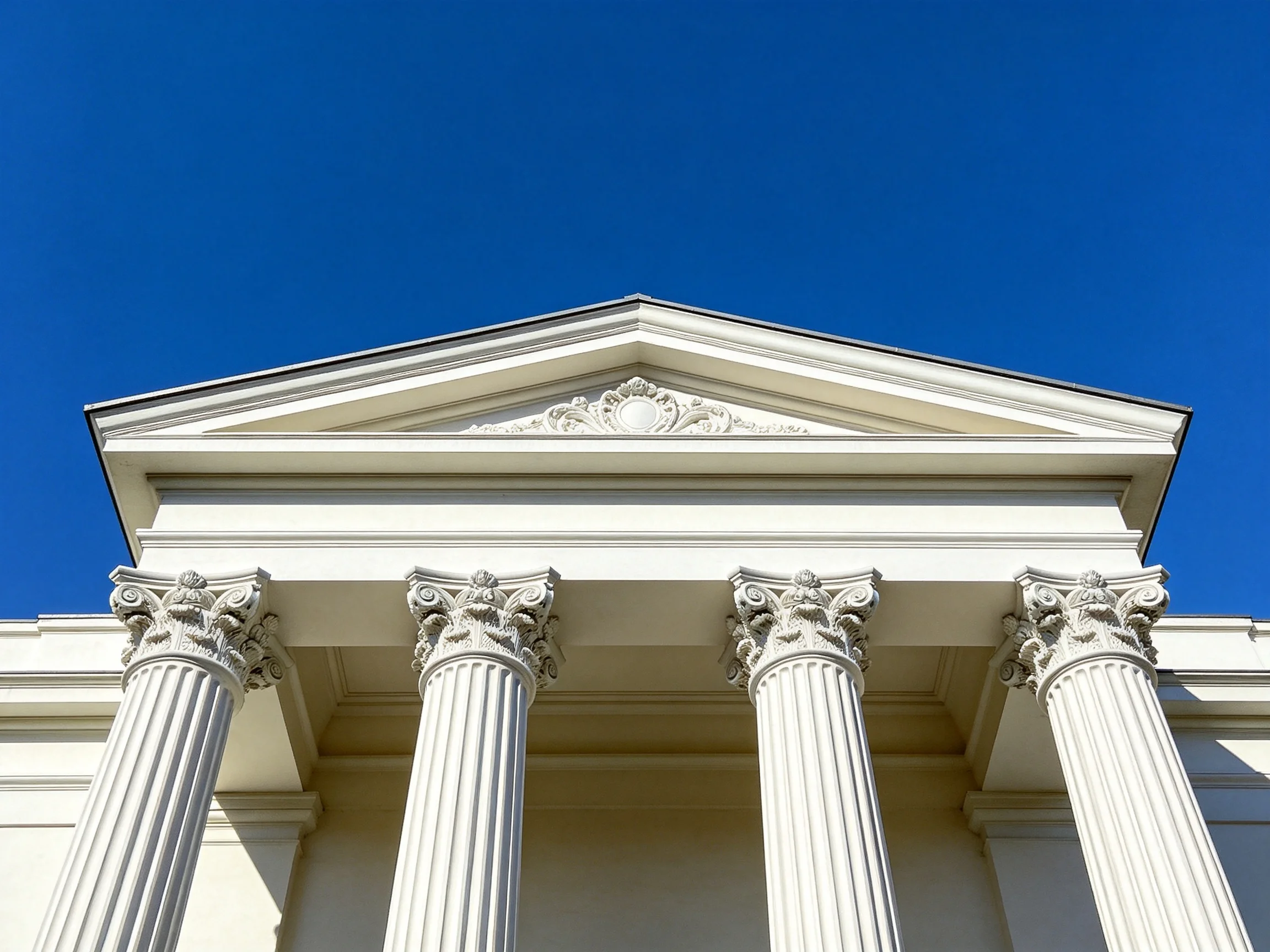 Four white columns with ornate capitals support a classical pediment under deep blue sky.