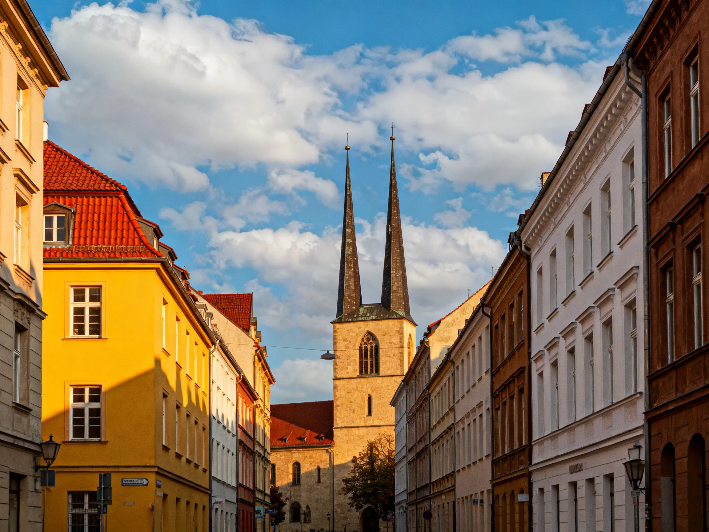 Historic buildings of varied colors border a street leading to a church tower with two