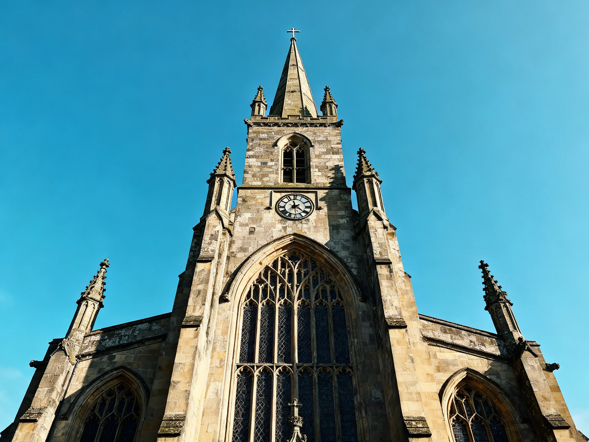 Historic stone church tower with clock and spire under bright blue sky