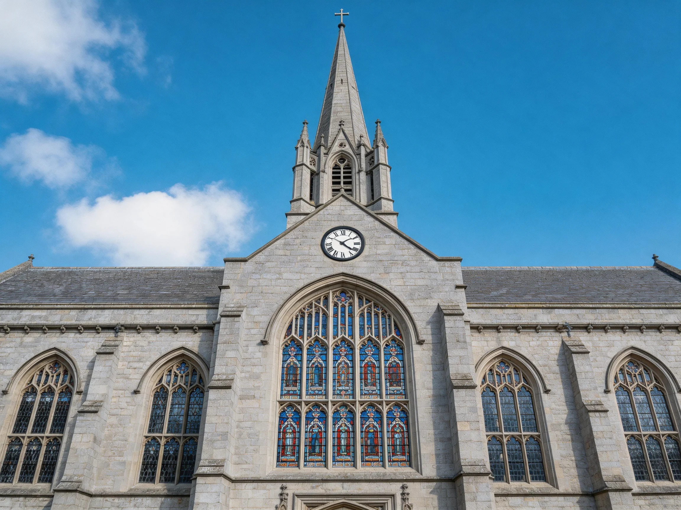 Historic stone church with tall spire, clock, and colorful stained glass
