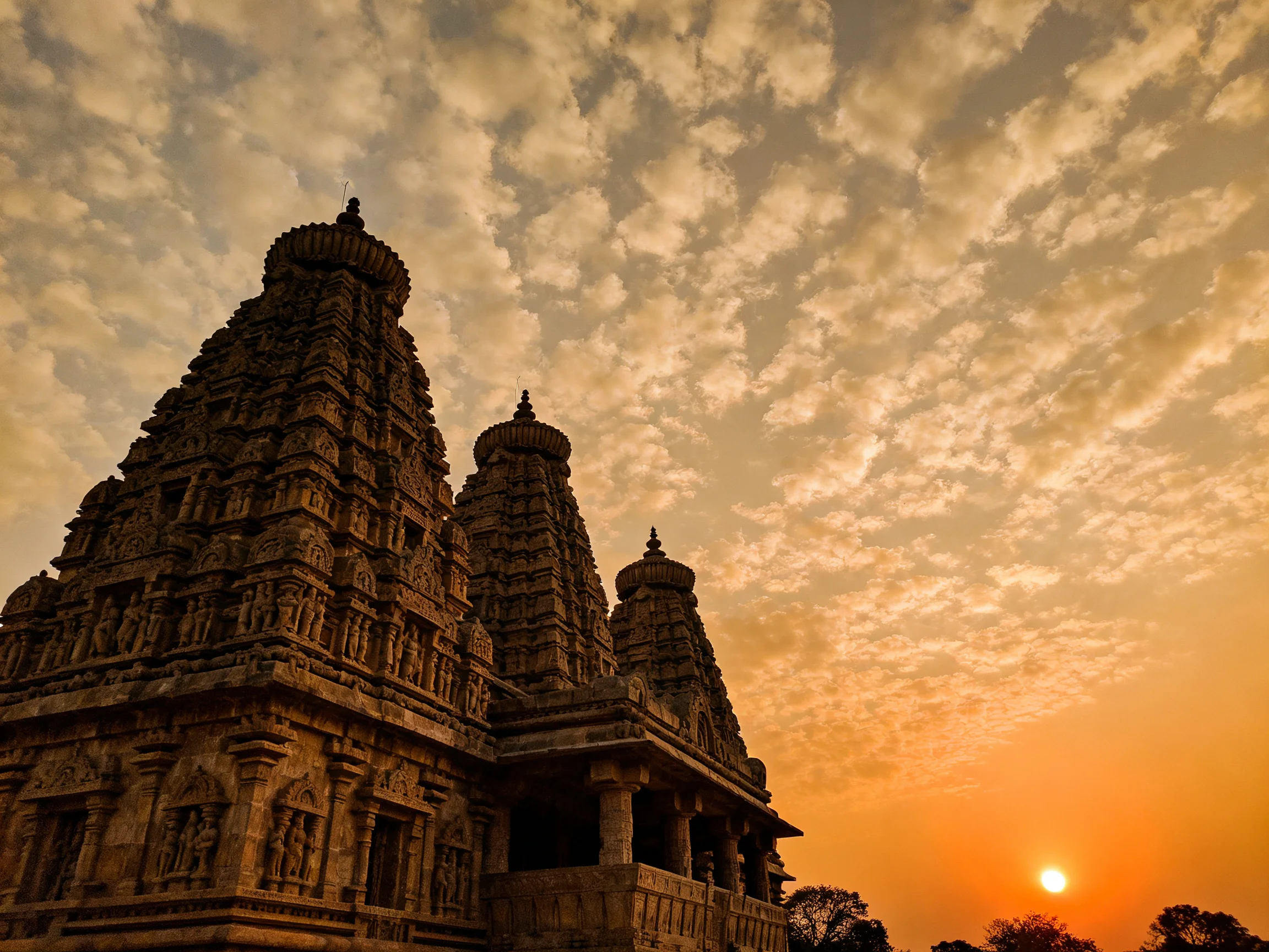 Intricate carved stone temples stand against a golden sunset sky