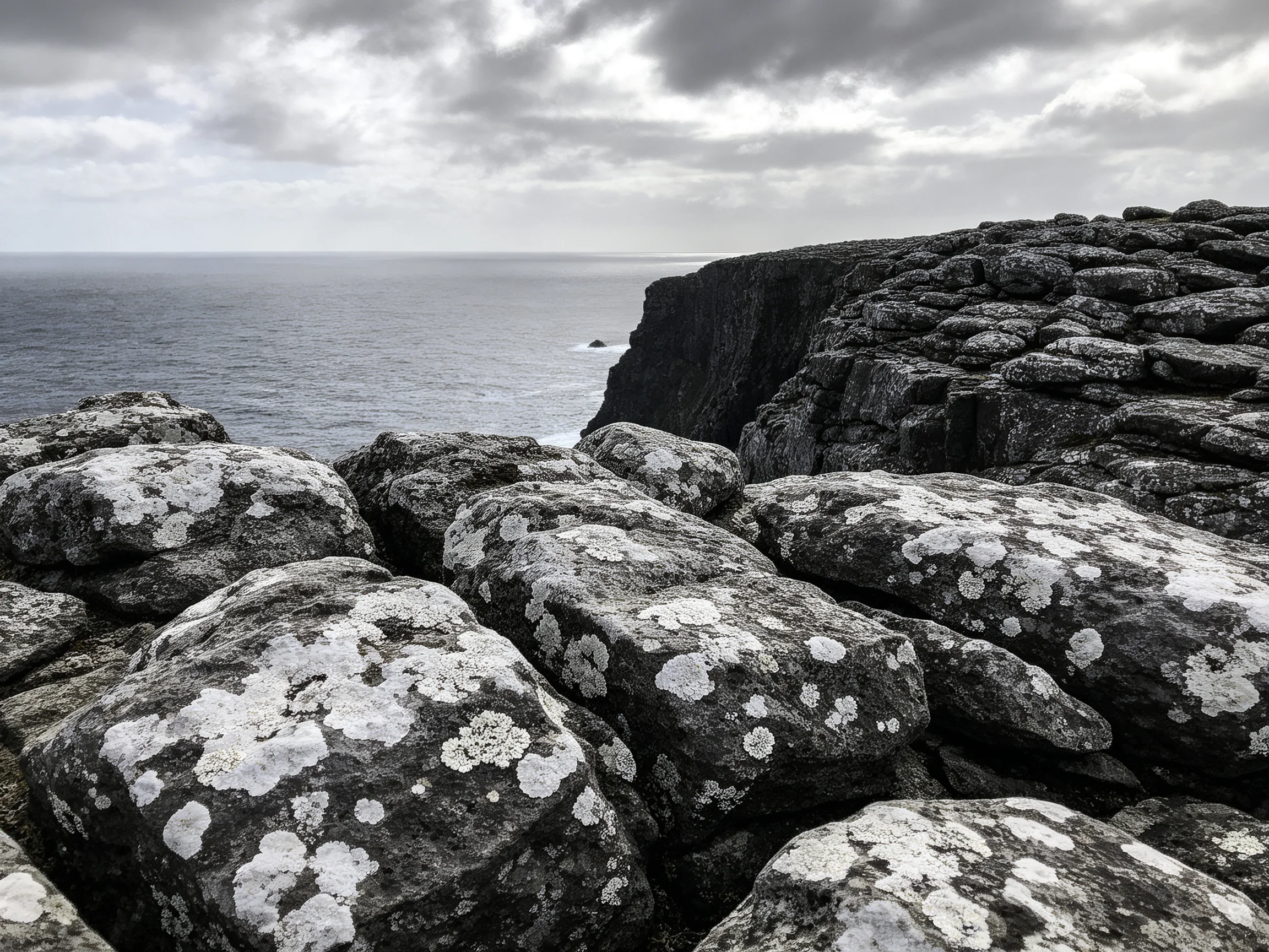 Lichen-covered rocks near cliffs overlook ocean under cloudy sky