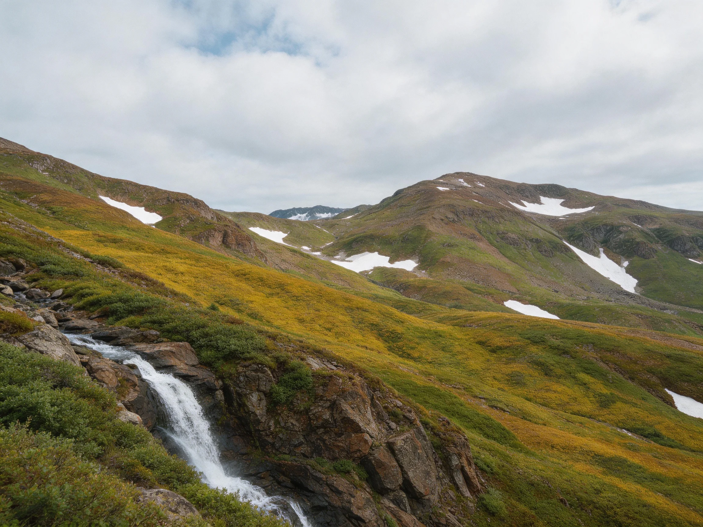 Rolling hills with cascading waterfall, vibrant green-yellow terrain, and scattered snow patches