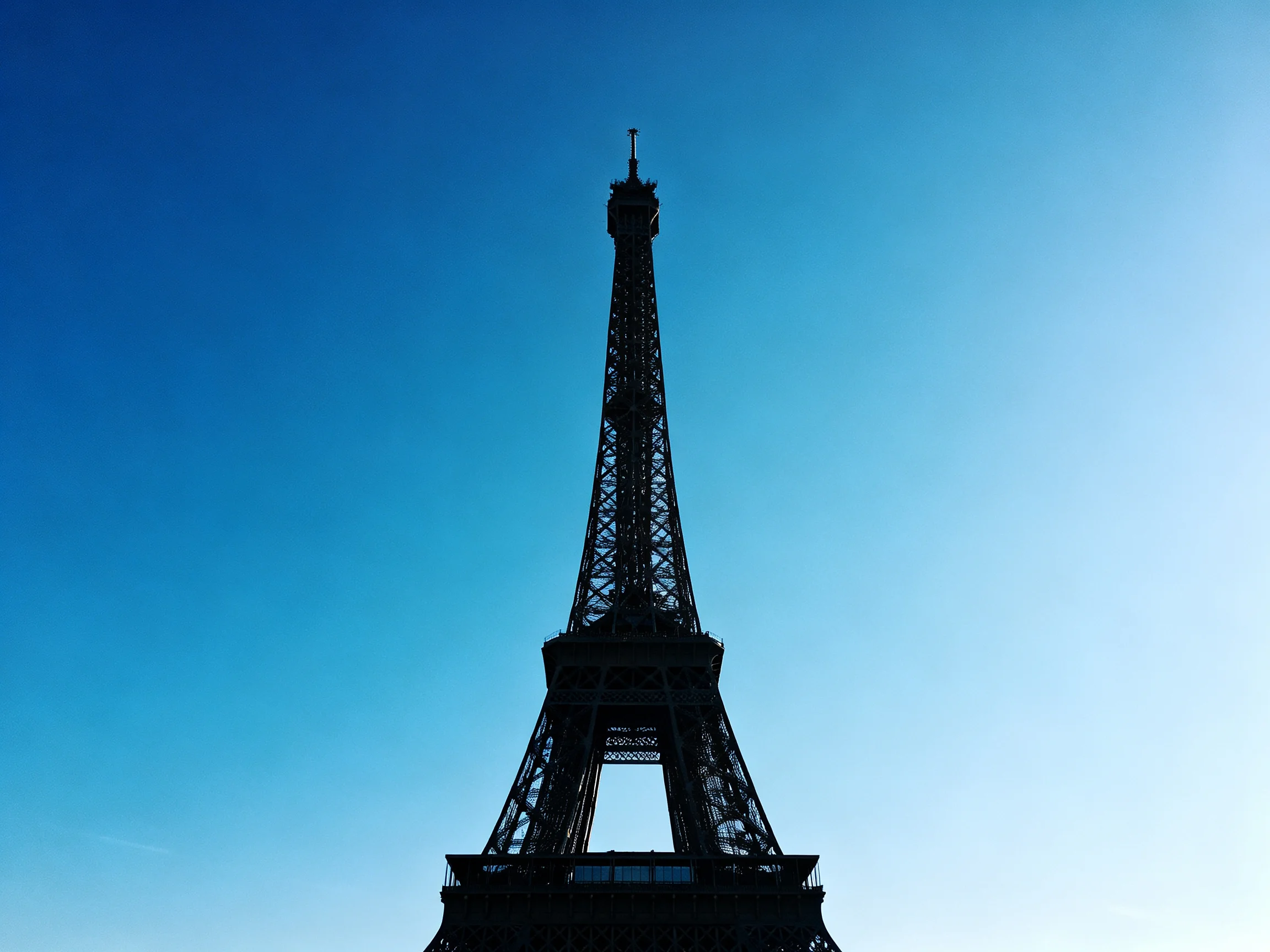 Silhouetted Eiffel Tower rises against vibrant blue sky backdrop