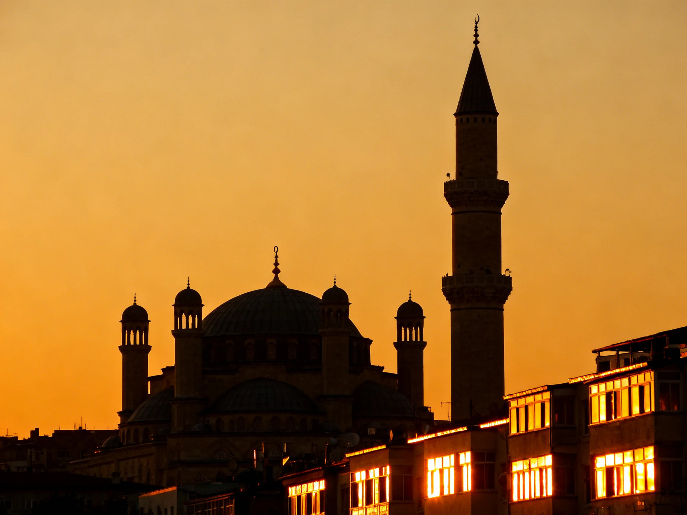 Silhouetted Mosque Complex with Minaret Under Warm Orange Sunset
