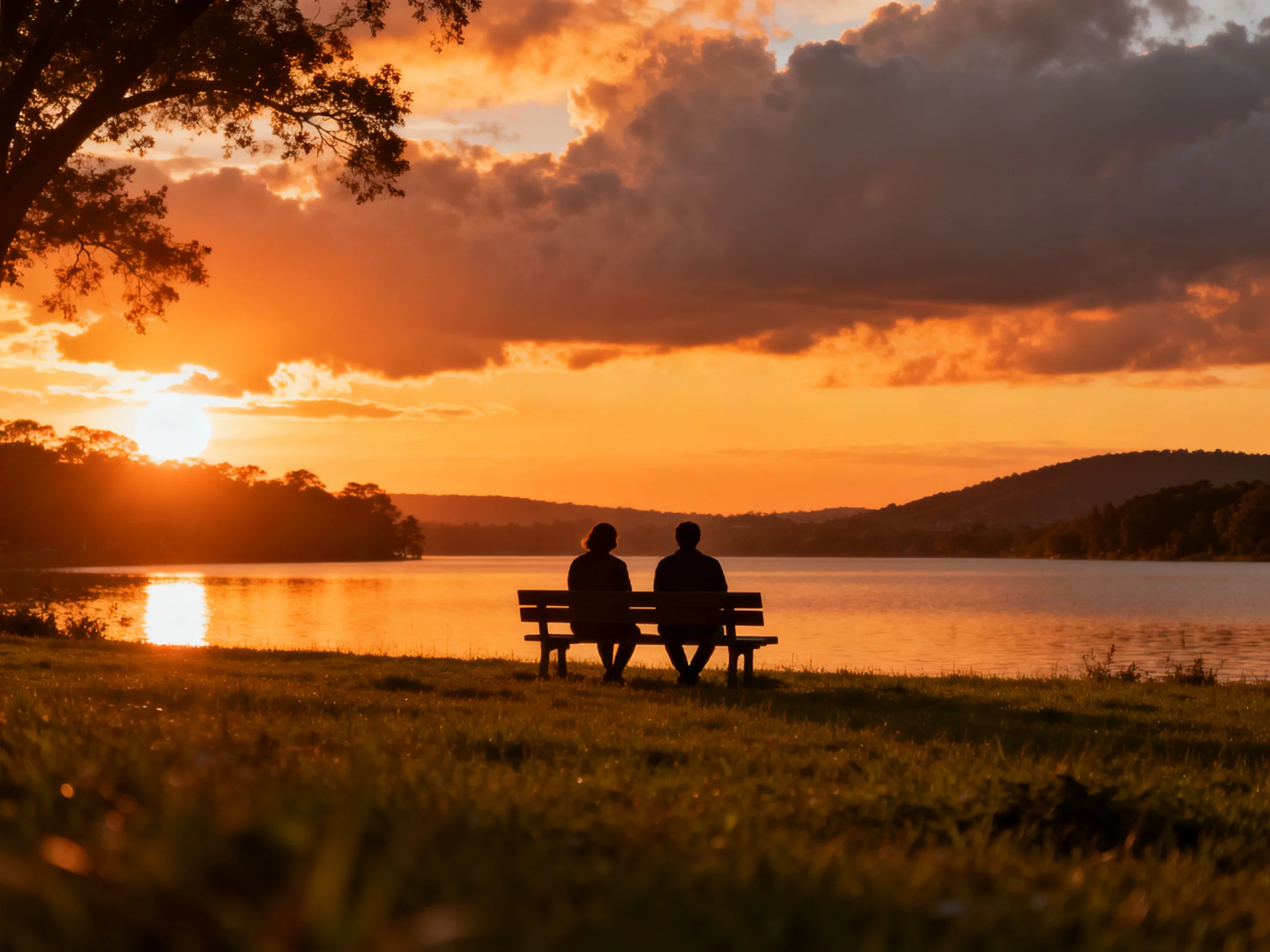 Silhouetted couple on bench viewing vibrant sunset over calm water