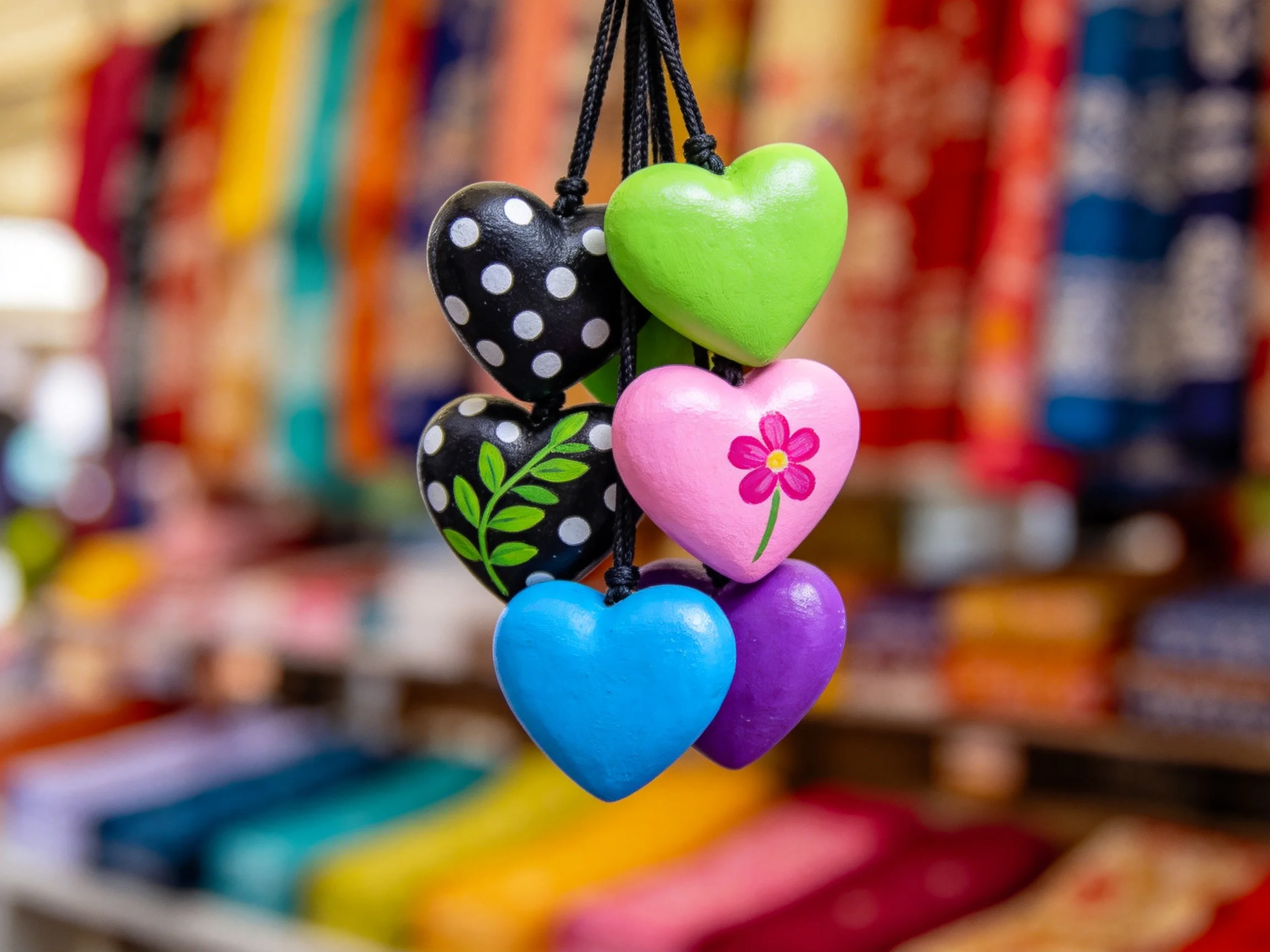 Six vibrant heart - shaped ornaments hang against a colorful textile backdrop