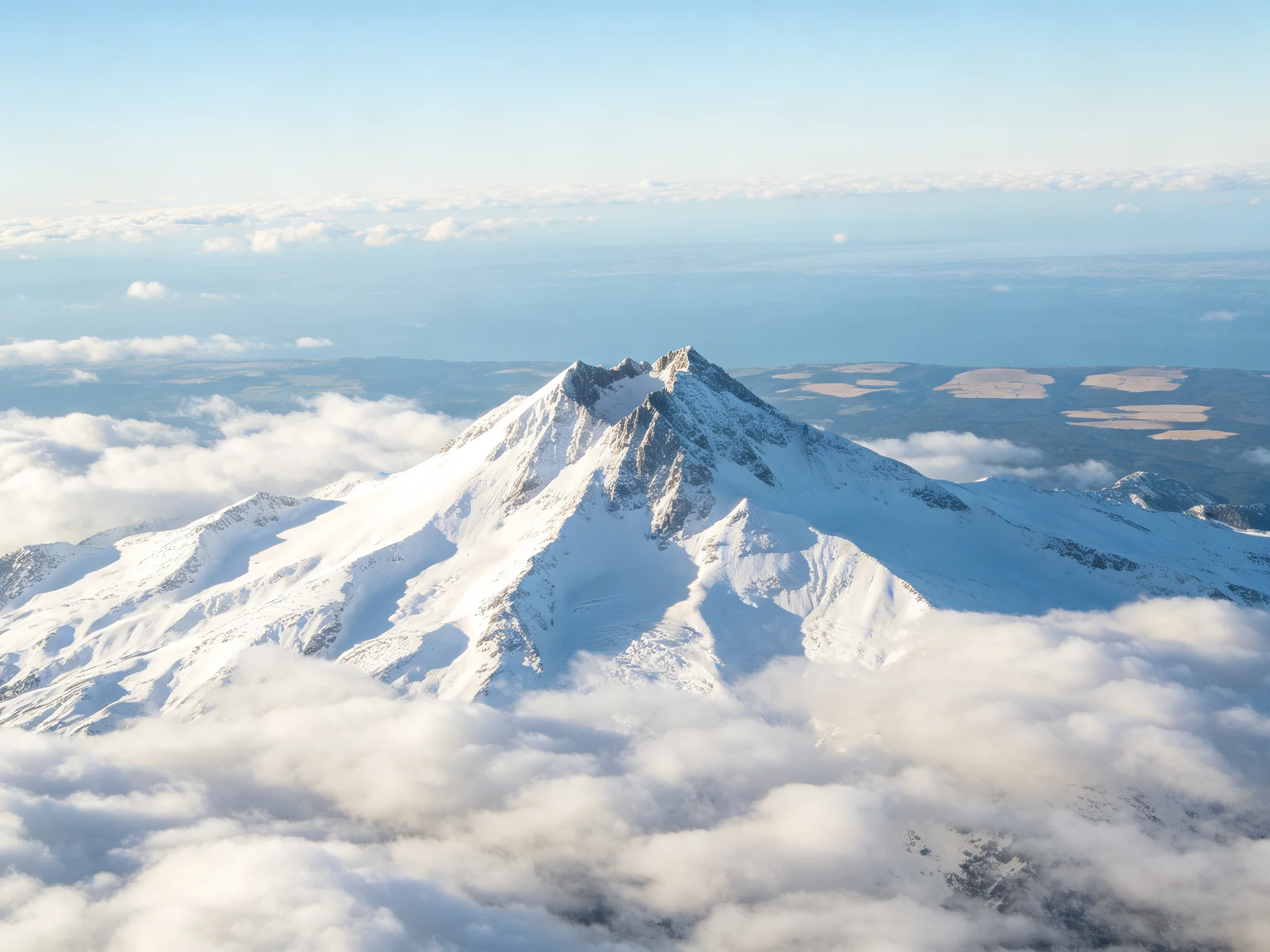 Snow-Capped Mountain Peak Rising Above Clouds with Distant Land