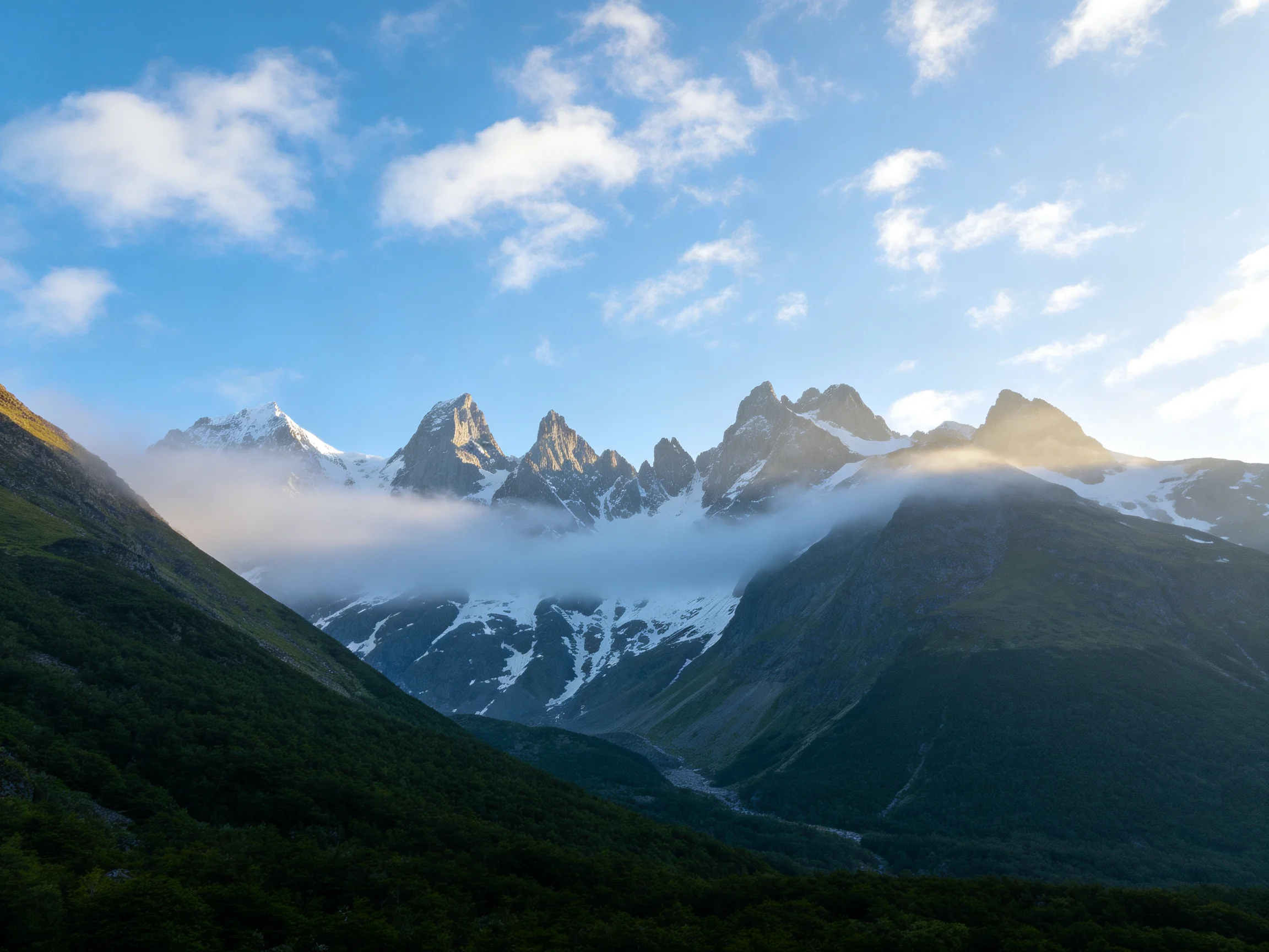 Snow-capped peaks rise behind misty clouds over lush valleys