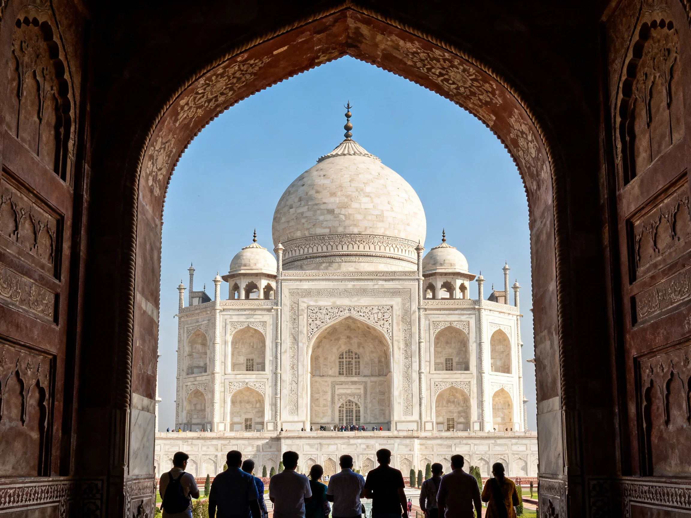 Taj Mahal viewed through ornate stone archway with visitors below