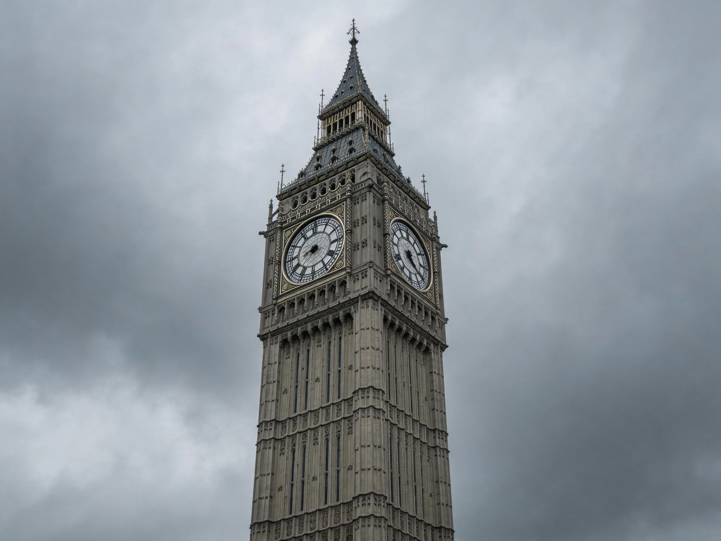 Tall historic clock tower with large clocks under gloomy skies
