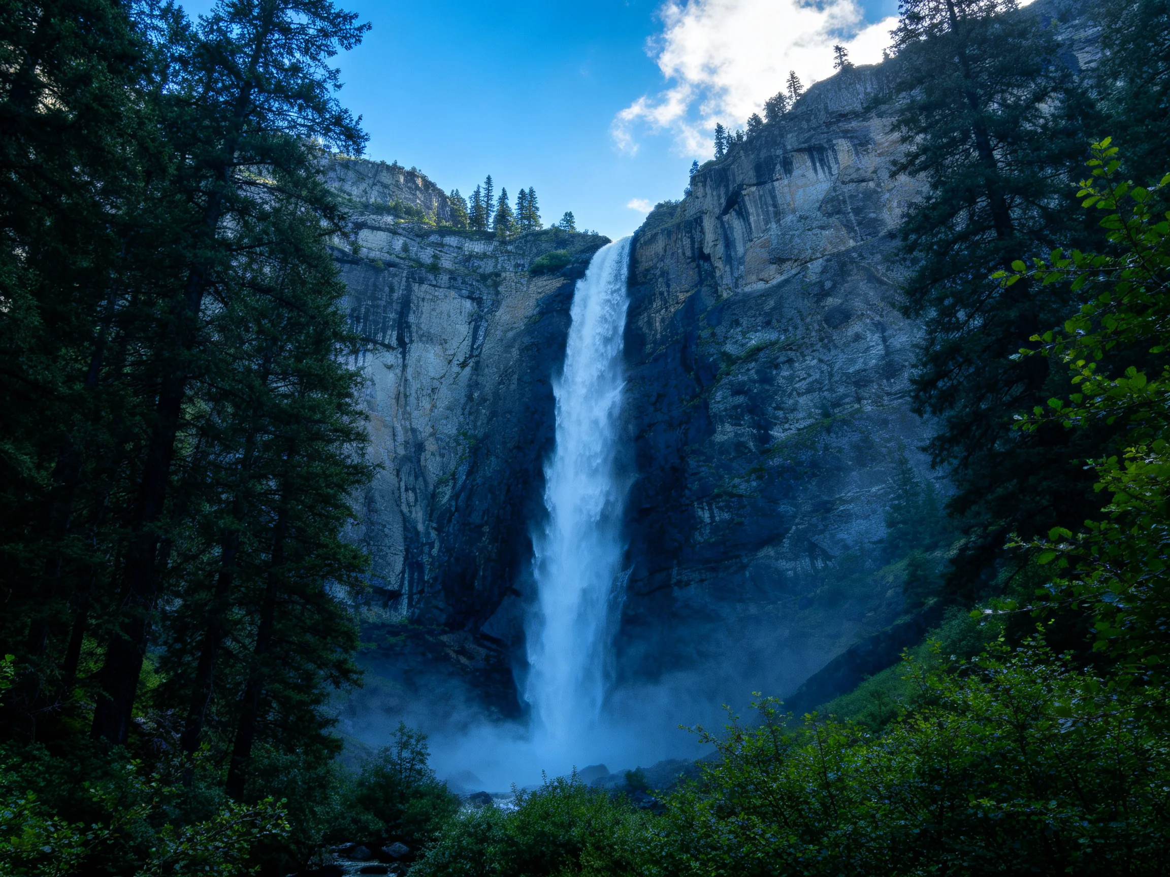 Tall waterfall cascades down rocky cliffs amid dense green forests