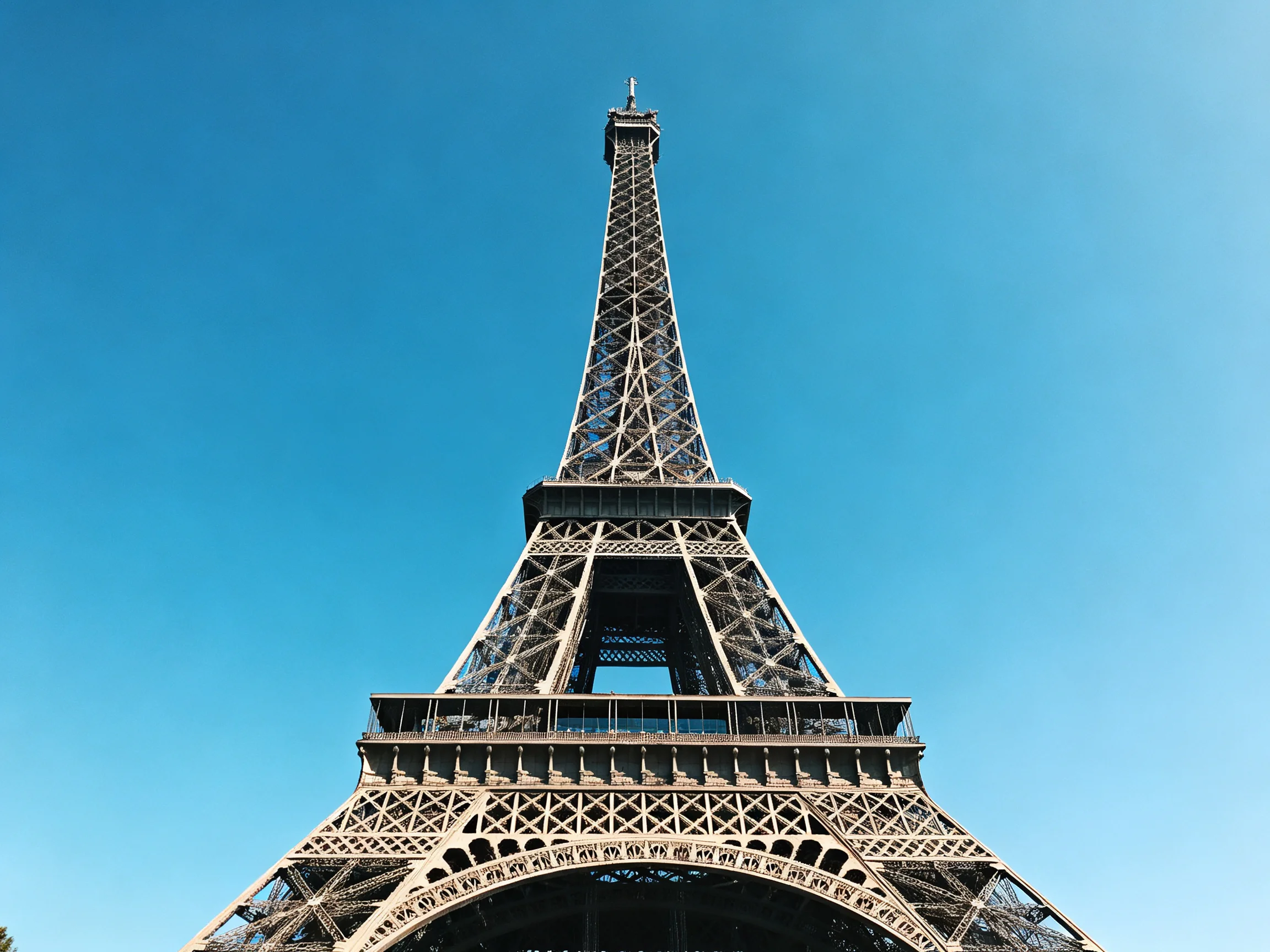 The Eiffel Towers metal lattice structure stands tall under a bright blue sky