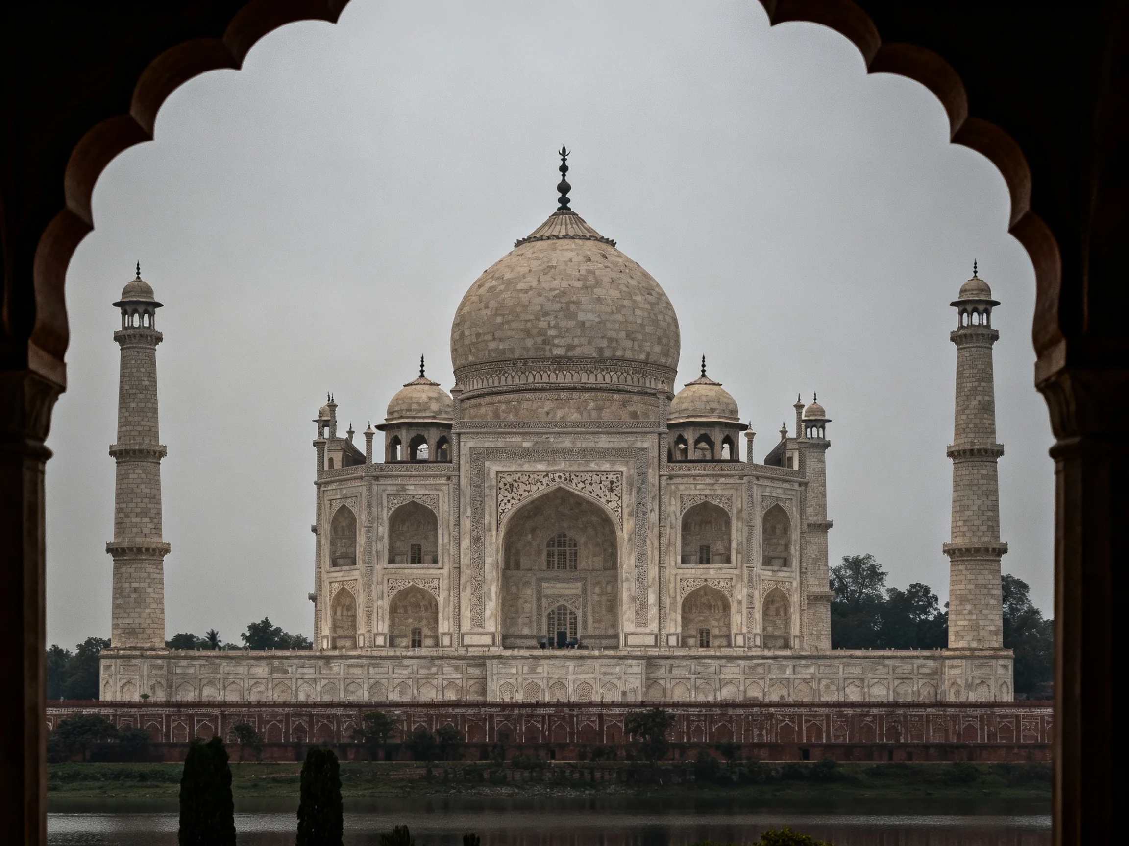 The Taj Mahal viewed through an ornate arch under a misty sky