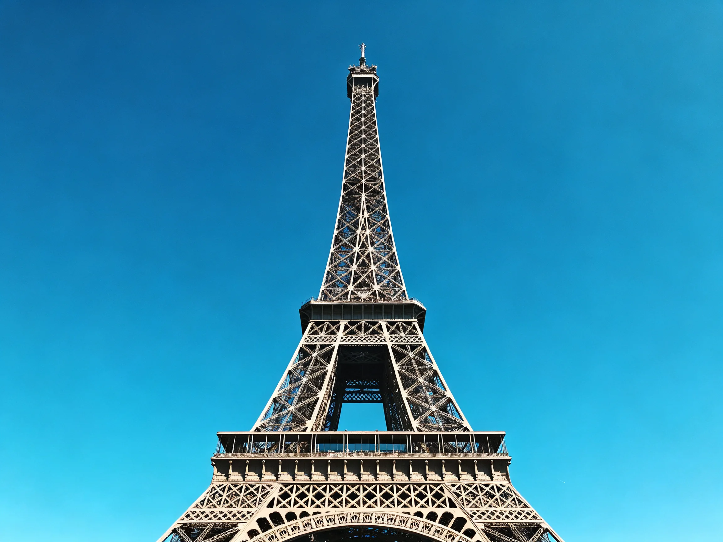 The grand iron lattice structure of the Eiffel Tower rises into a vivid blue sky.