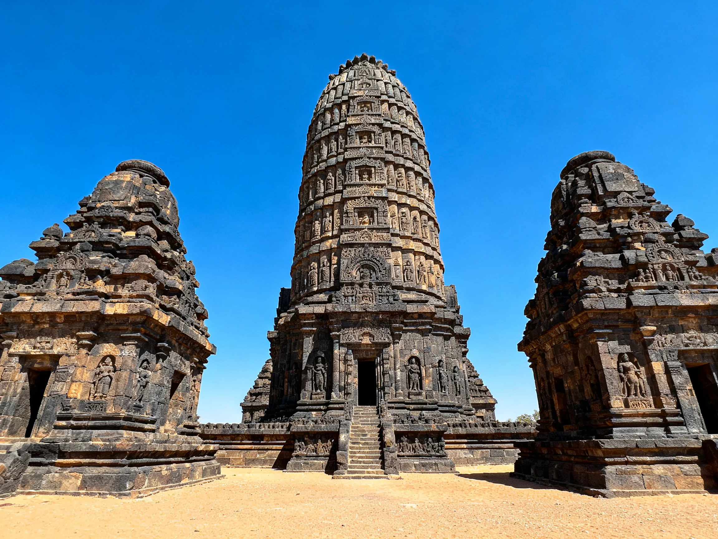 Three ancient stone temple structures with intricate carvings under a clear blue sky