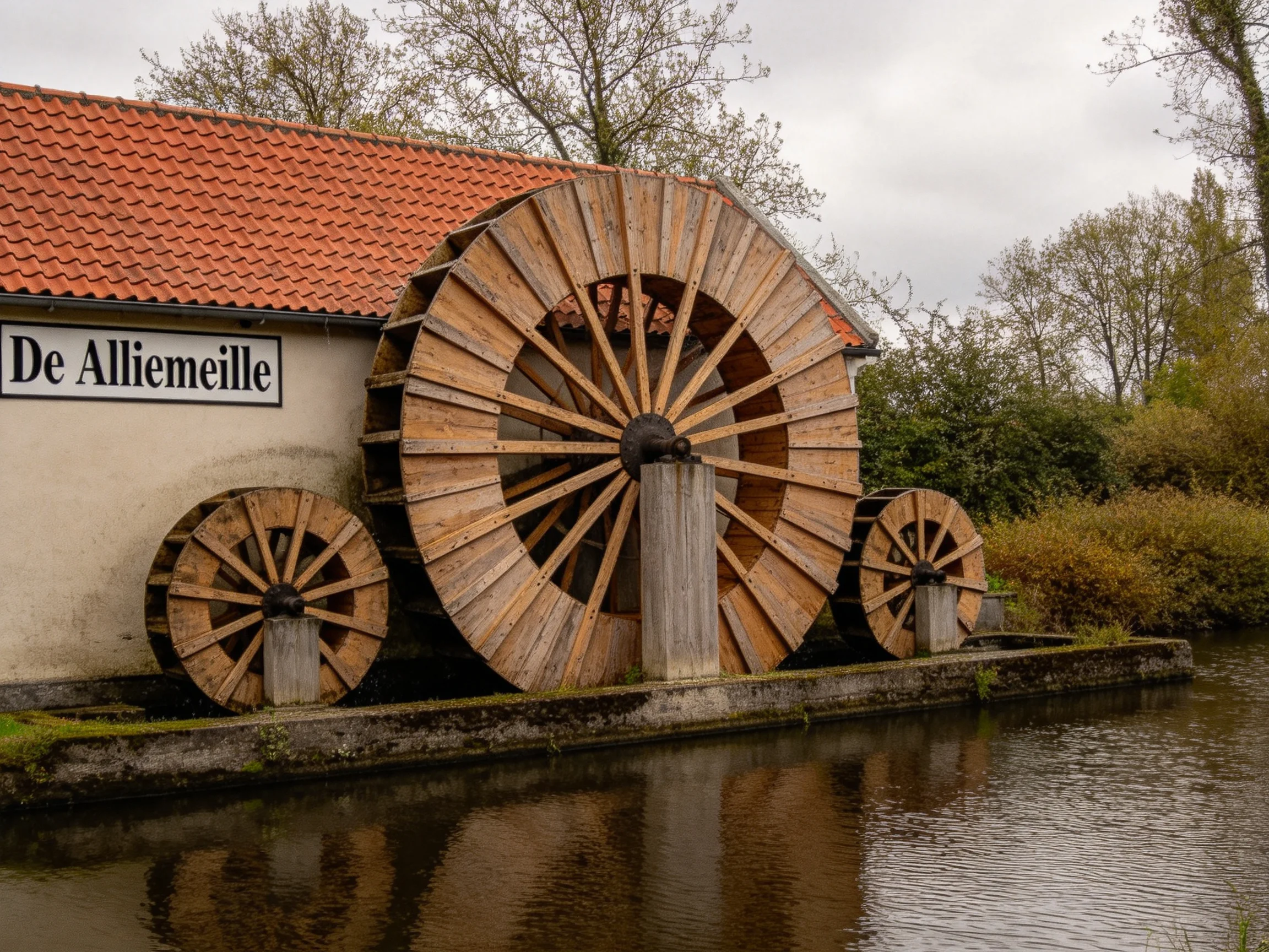 Three large wooden waterwheels beside a building with red roof