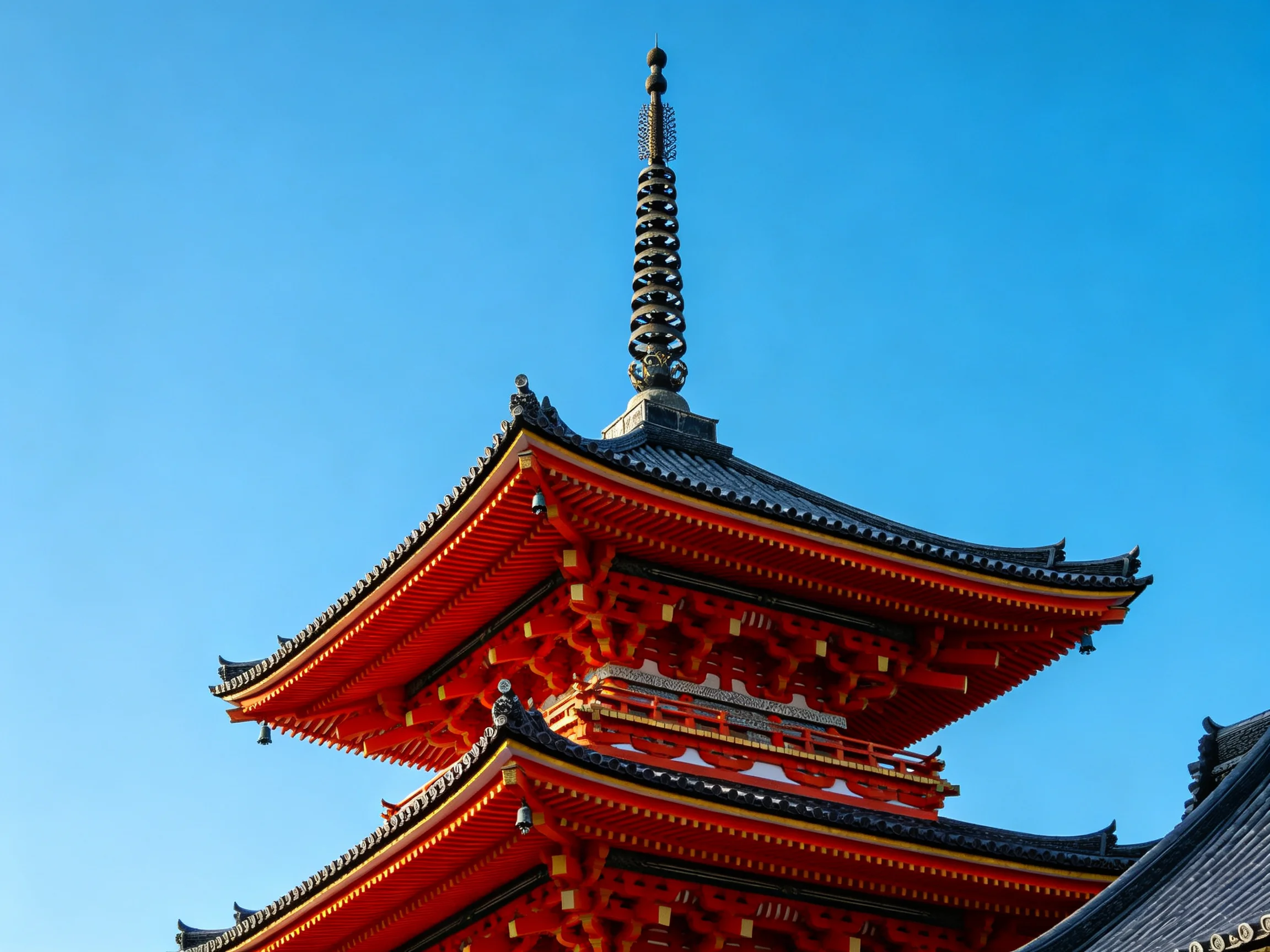 Three-tiered red pagoda with ornate spire under bright blue sky