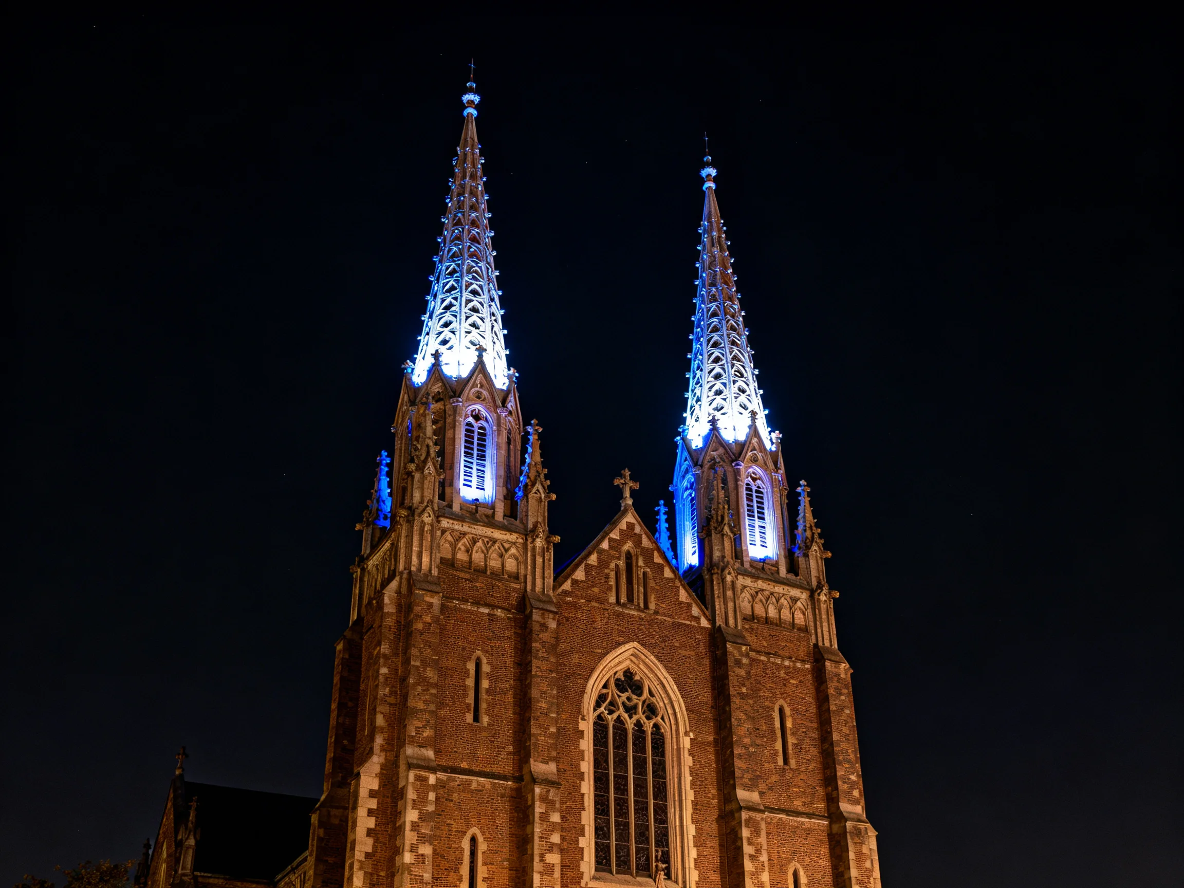 Twin Gothic spires lit in blue on a brick cathedral at night